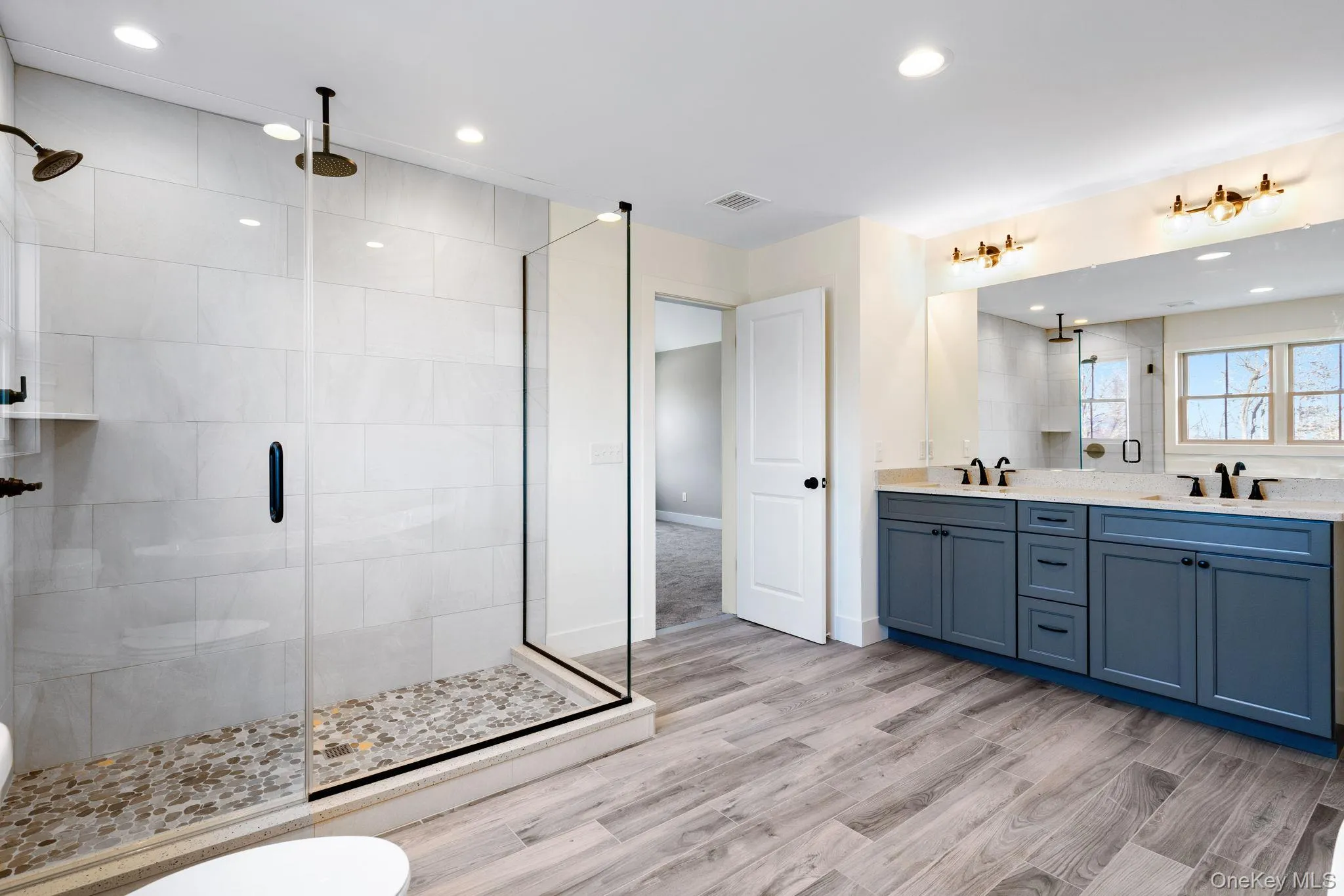 Bathroom featuring double vanity, a stall shower, recessed lighting, and light wood-style floors Bathroom featuring double vanity, a stall shower, recessed lighting, and light wood-style floors