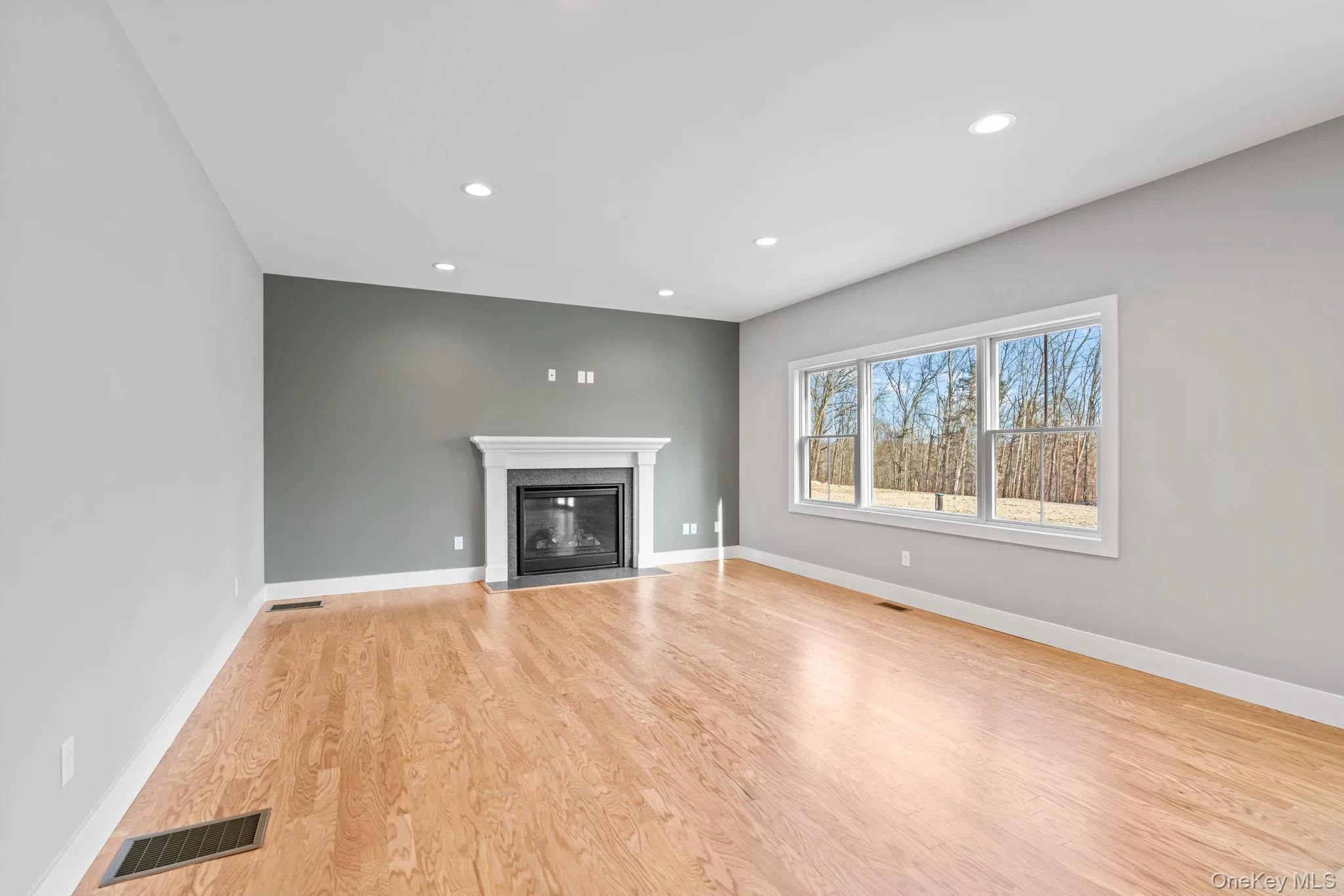 Unfurnished living room featuring light wood-type flooring, a fireplace with flush hearth, and recessed lighting Unfurnished living room featuring light wood-type flooring, a fireplace with flush hearth, and recessed lighting