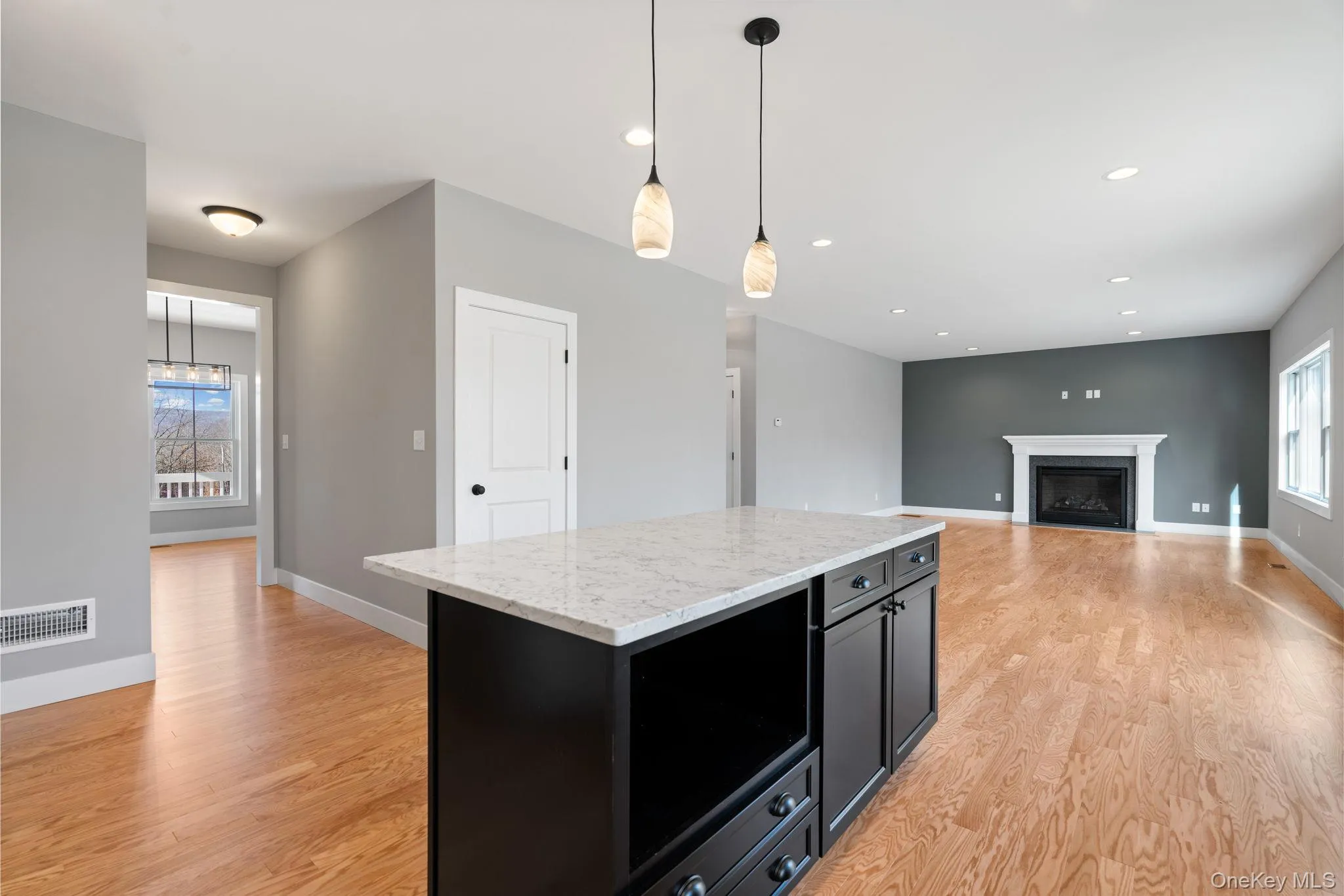 Kitchen featuring dark cabinetry, hanging light fixtures, light wood finished floors, light stone counters, and a fireplace Kitchen featuring dark cabinetry, hanging light fixtures, light wood finished floors, light stone counters, and a fireplace