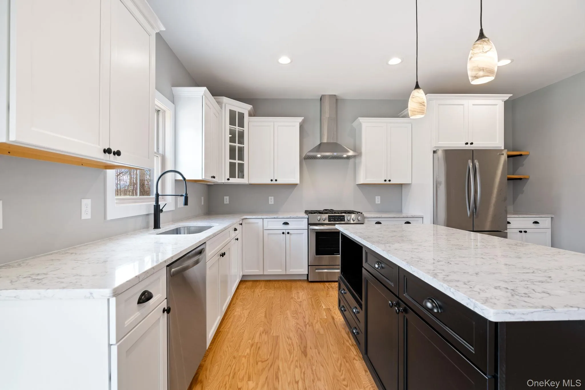 Kitchen with glass insert cabinets, white cabinets, stainless steel appliances, wall chimney range hood, and pendant lighting Kitchen with glass insert cabinets, white cabinets, stainless steel appliances, wall chimney range hood, and pendant lighting