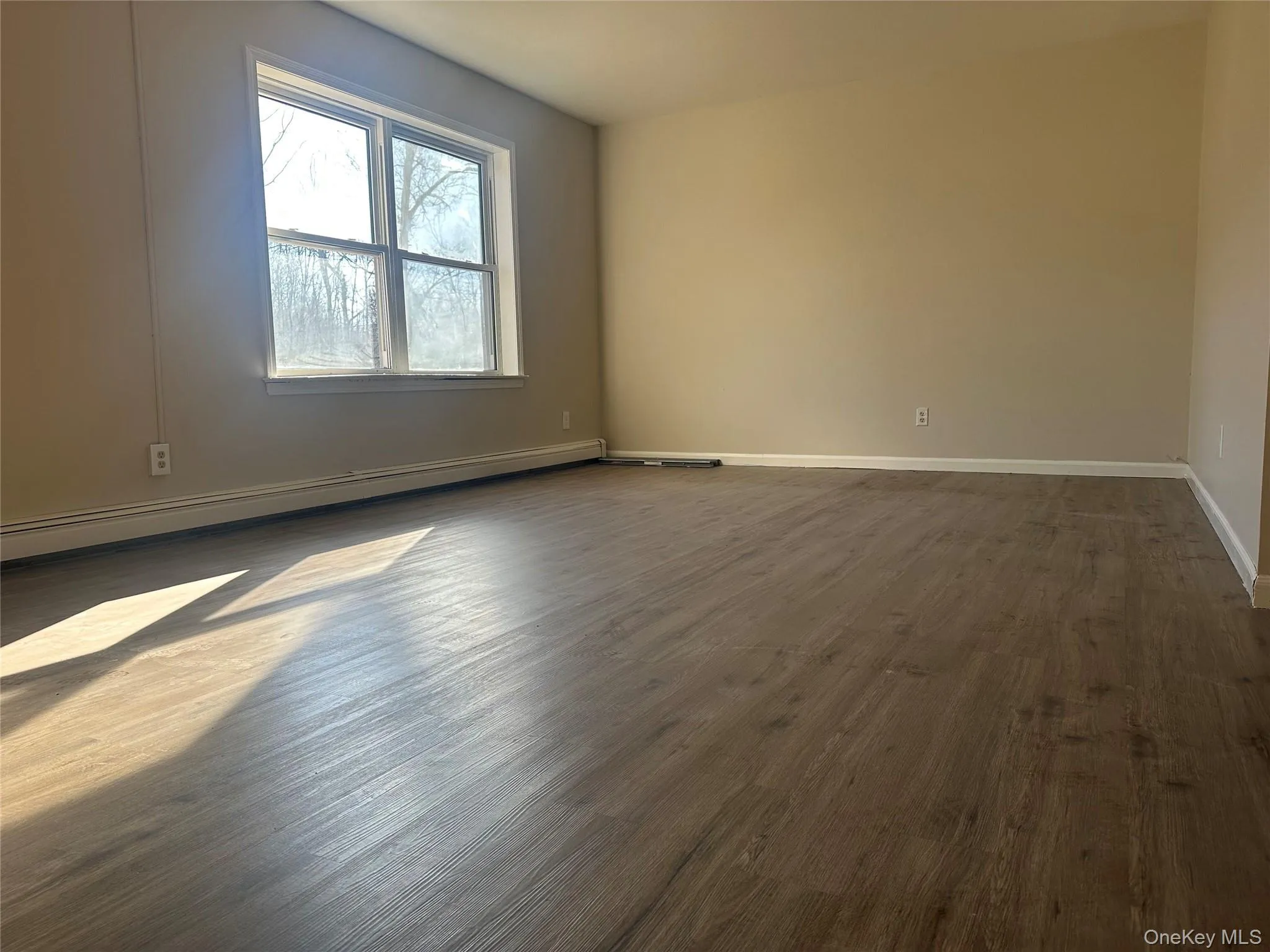 Empty room with a baseboard heating unit and dark wood-style floors Empty room with a baseboard heating unit and dark wood-style floors