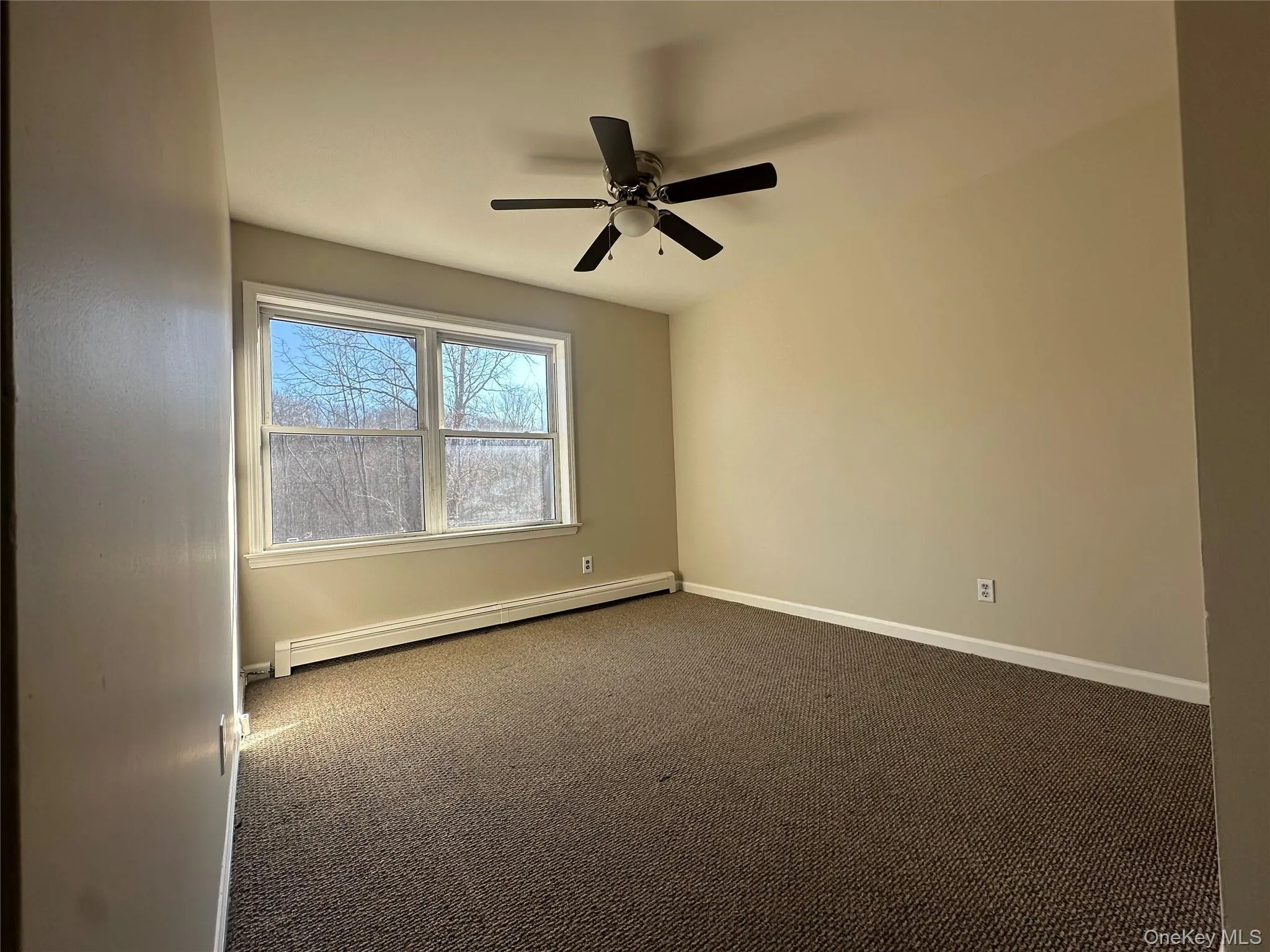 Carpeted empty room with a baseboard radiator and a ceiling fan Carpeted empty room with a baseboard radiator and a ceiling fan