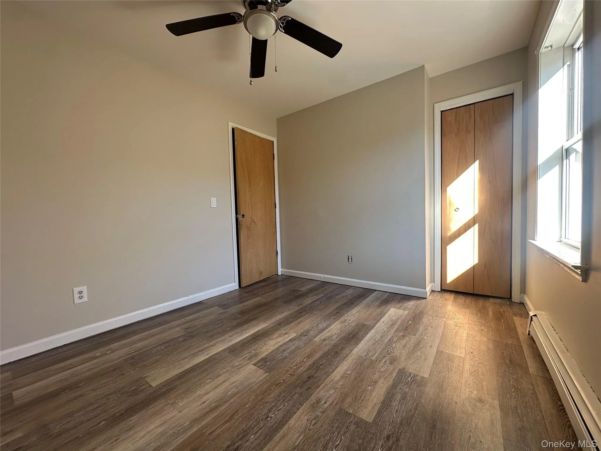 Unfurnished room featuring baseboard heating, dark wood-type flooring, and a ceiling fan Unfurnished room featuring baseboard heating, dark wood-type flooring, and a ceiling fan