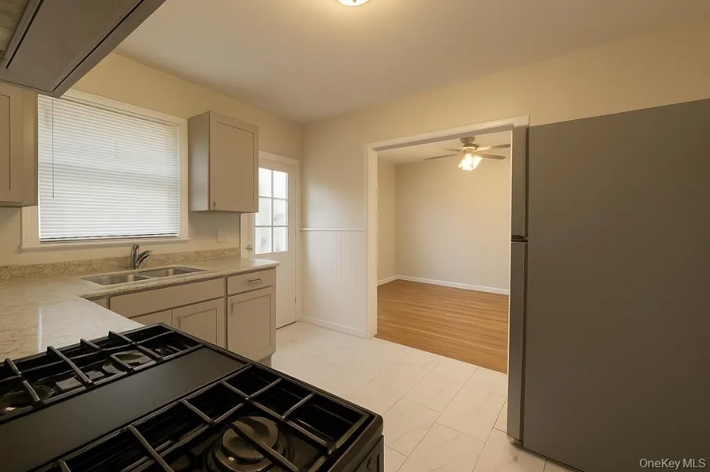 Kitchen featuring freestanding refrigerator, gas stove, extractor fan, light stone counters, and ceiling fan Kitchen featuring freestanding refrigerator, gas stove, extractor fan, light stone counters, and ceiling fan