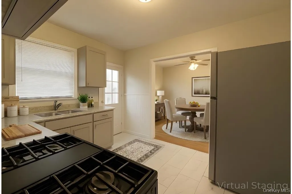 Kitchen with freestanding refrigerator, black gas stove, a wainscoted wall, light stone counters, and ceiling fan Kitchen with freestanding refrigerator, black gas stove, a wainscoted wall, light stone counters, and ceiling fan