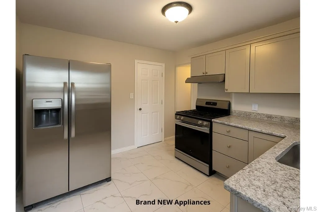 Kitchen featuring stainless steel appliances, light marble finish flooring, under cabinet range hood, and light stone countertops Kitchen featuring stainless steel appliances, light marble finish flooring, under cabinet range hood, and light stone countertops