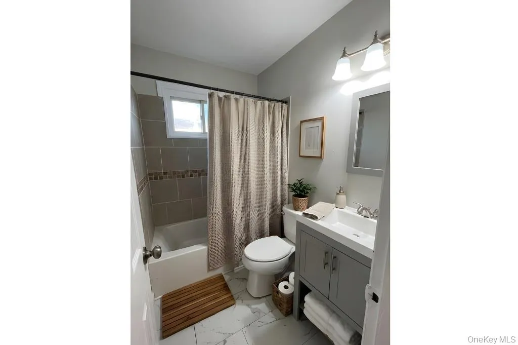 Full bathroom featuring shower / bath combo with shower curtain, vanity, and light marble finish floors Full bathroom featuring shower / bath combo with shower curtain, vanity, and light marble finish floors