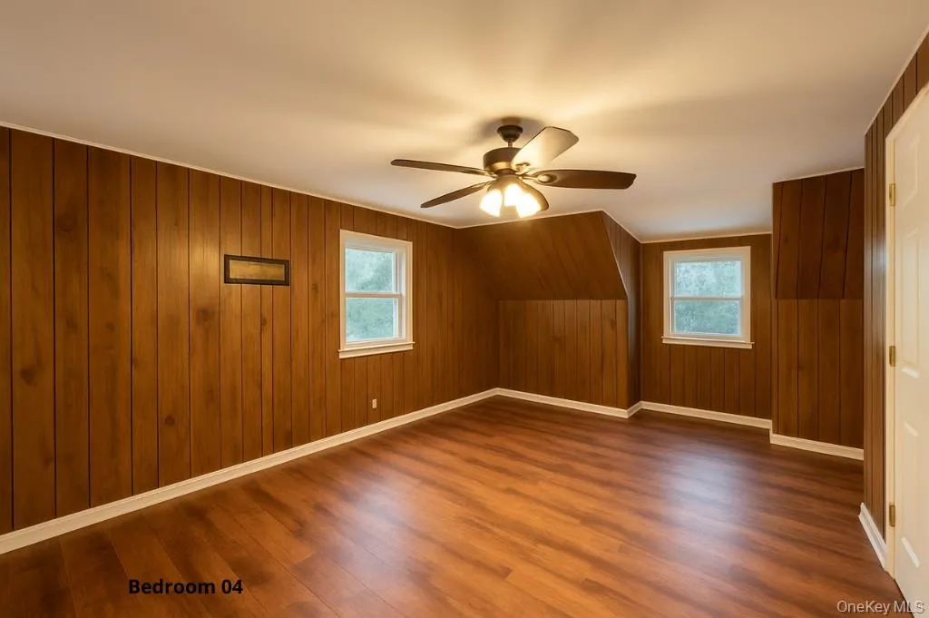 Additional living space with a ceiling fan, dark wood-type flooring, wood walls, and plenty of natural light Additional living space with a ceiling fan, dark wood-type flooring, wood walls, and plenty of natural light