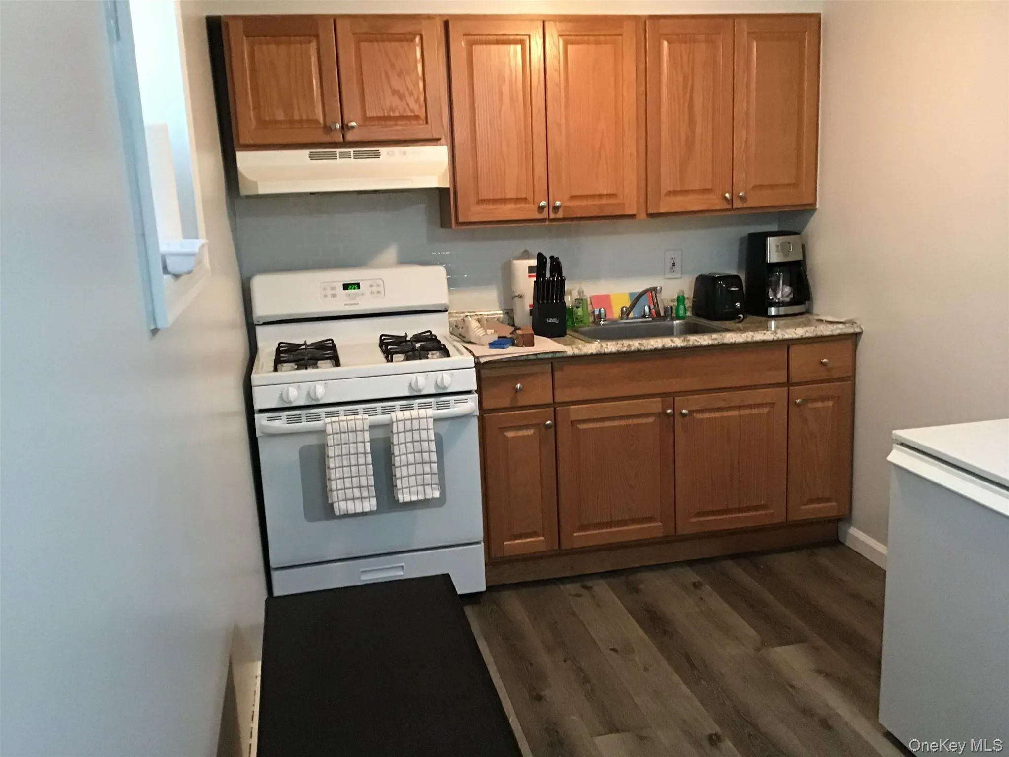Kitchen with white range with gas cooktop, brown cabinets, under cabinet range hood, and dark wood-type flooring Kitchen with white range with gas cooktop, brown cabinets, under cabinet range hood, and dark wood-type flooring