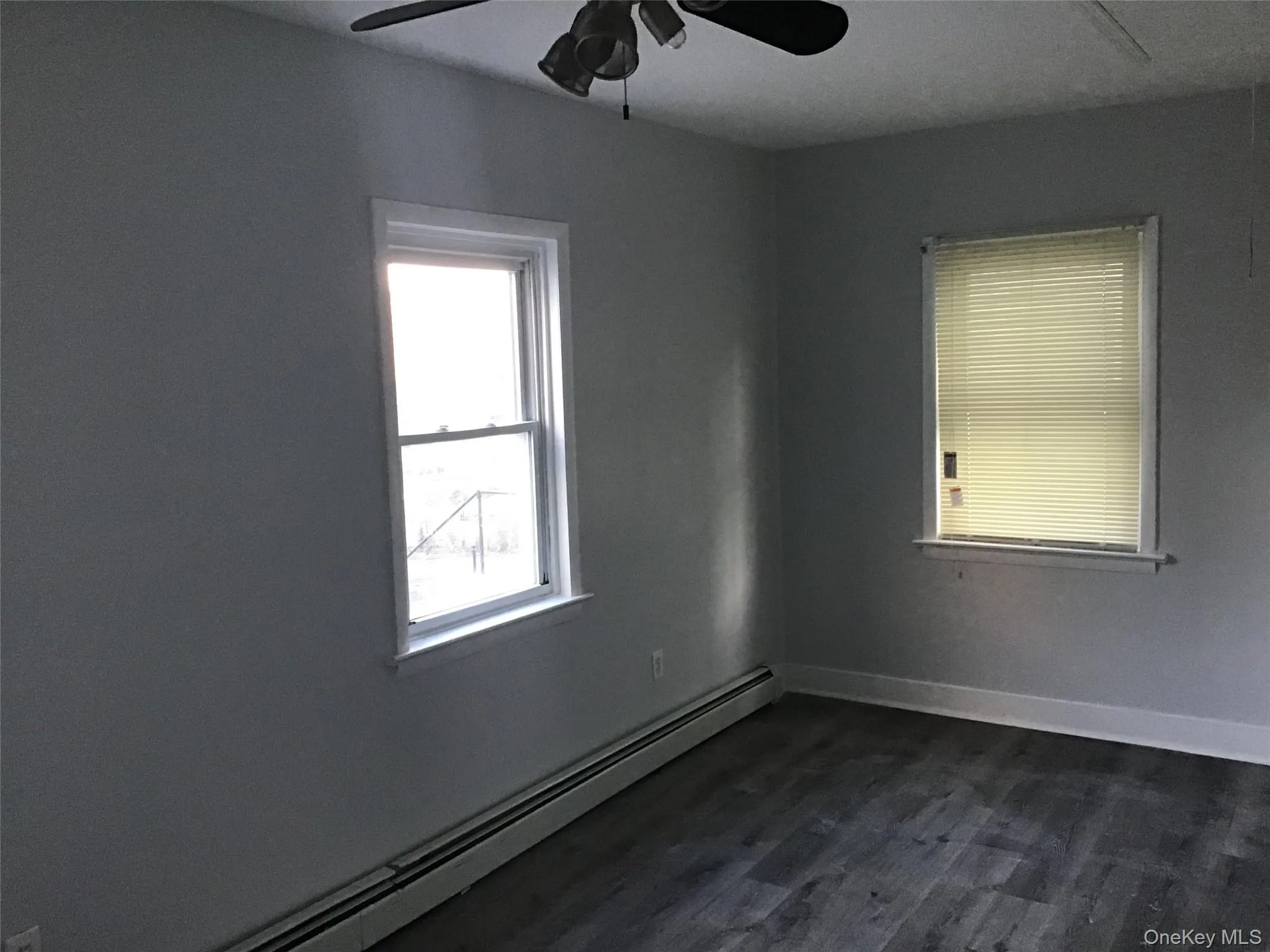 Empty room with a baseboard heating unit, a ceiling fan, and dark wood-style flooring Empty room with a baseboard heating unit, a ceiling fan, and dark wood-style flooring