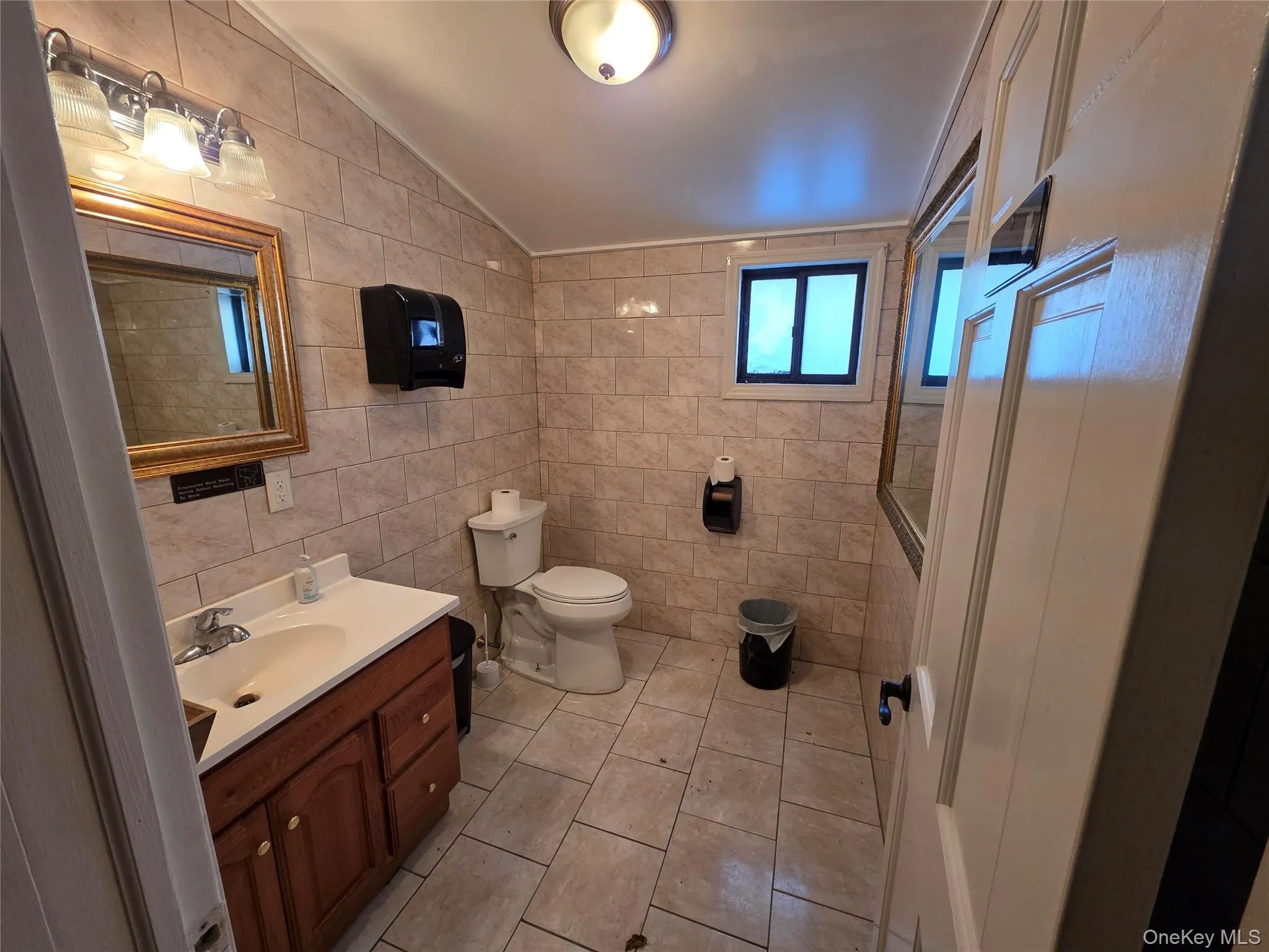 Full bathroom featuring tile walls, vaulted ceiling, vanity, and light tile patterned floors Full bathroom featuring tile walls, vaulted ceiling, vanity, and light tile patterned floors
