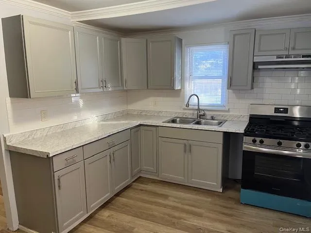 Kitchen with gray cabinetry, gas range, light countertops, decorative backsplash, and crown molding Kitchen with gray cabinetry, gas range, light countertops, decorative backsplash, and crown molding