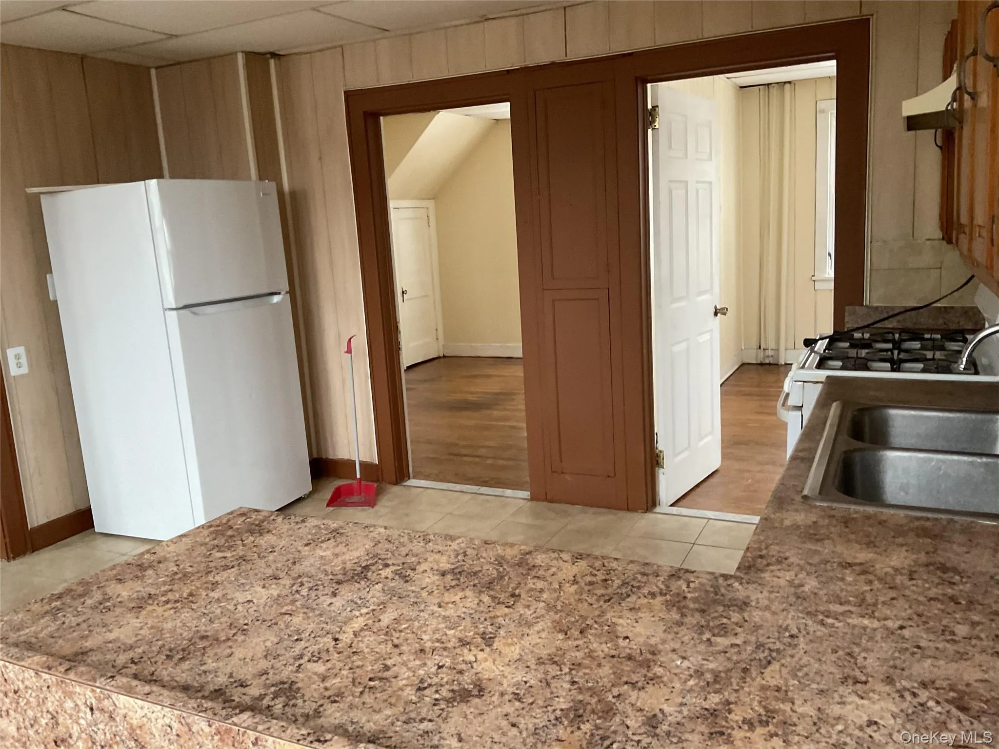 Kitchen featuring white appliances, range hood, light tile patterned floors, and wooden walls Kitchen featuring white appliances, range hood, light tile patterned floors, and wooden walls
