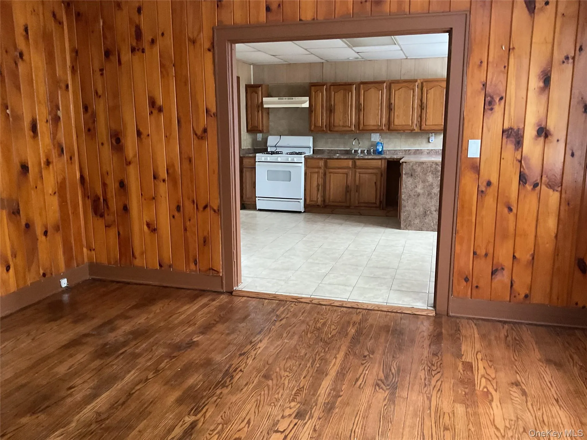 Kitchen featuring brown cabinetry, white gas range, wood walls, under cabinet range hood, and light wood-type flooring Kitchen featuring brown cabinetry, white gas range, wood walls, under cabinet range hood, and light wood-type flooring