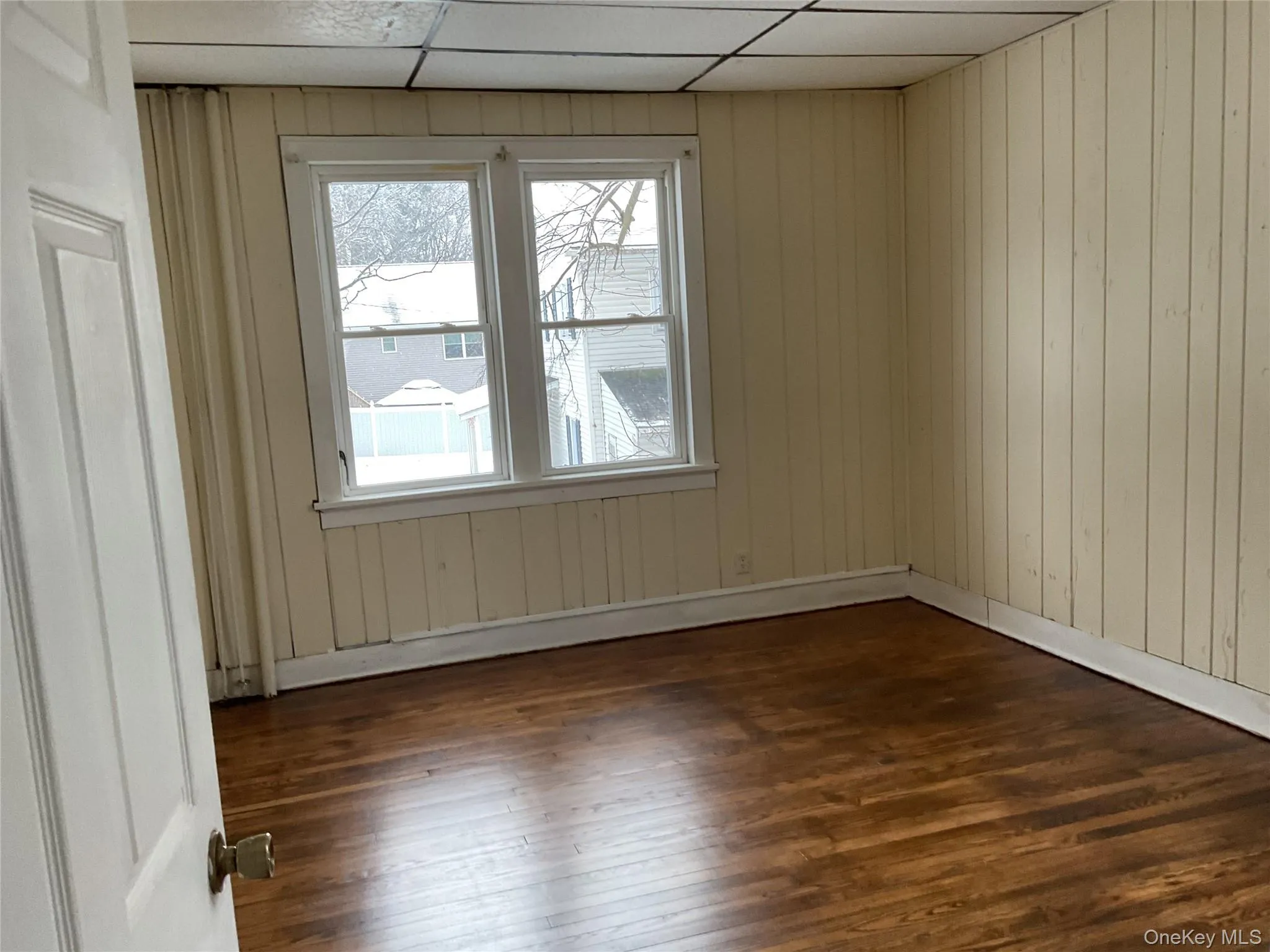 Unfurnished room featuring dark wood-type flooring, wood walls, and a drop ceiling Unfurnished room featuring dark wood-type flooring, wood walls, and a drop ceiling