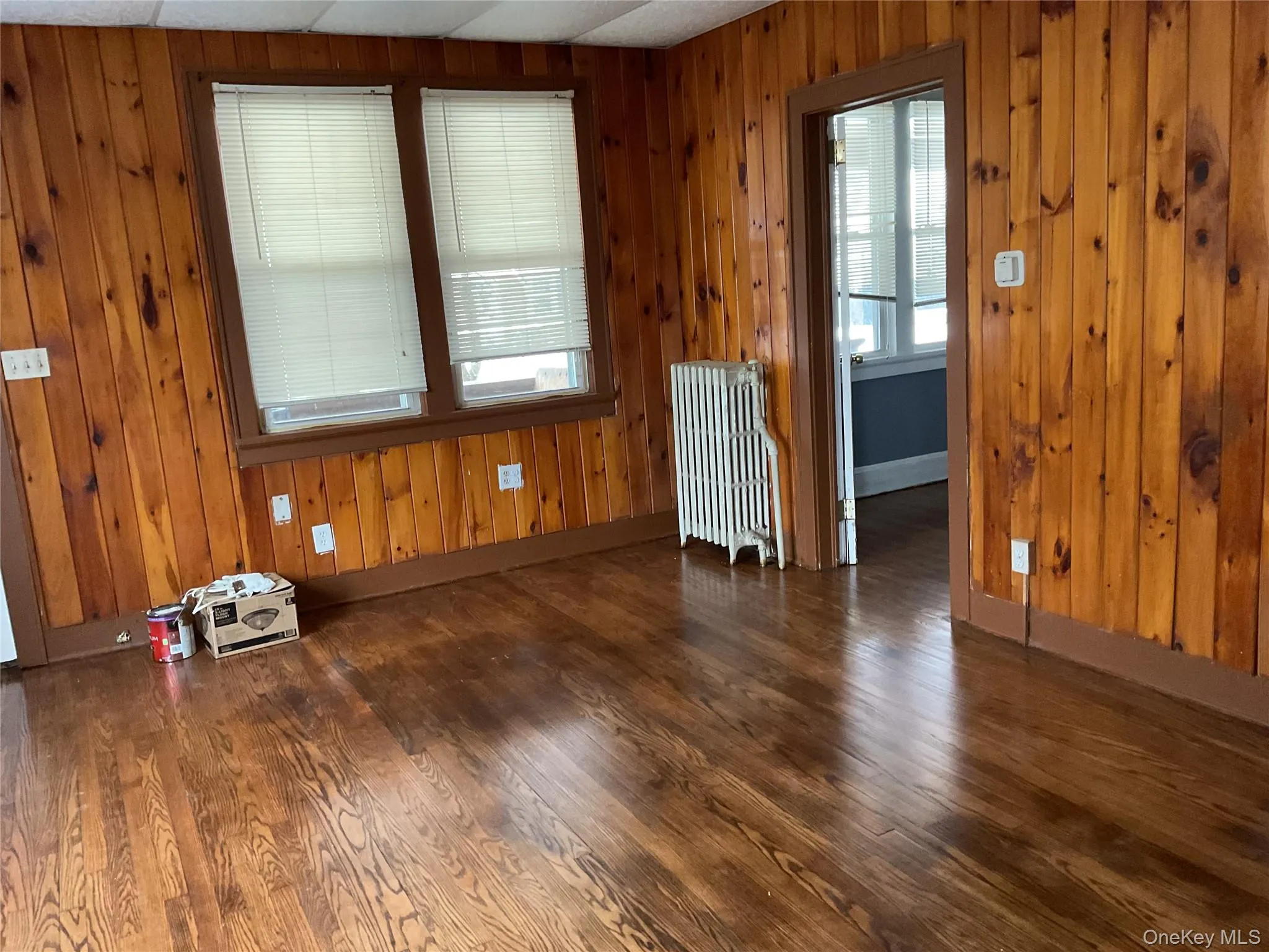 Empty room with radiator heating unit, dark wood-style flooring, and wood walls Empty room with radiator heating unit, dark wood-style flooring, and wood walls
