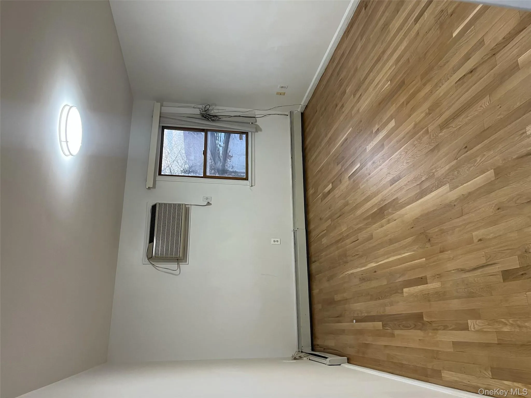 Unfurnished room with light wood-style flooring, baseboard heating, and a wall mounted AC Unfurnished room with light wood-style flooring, baseboard heating, and a wall mounted AC
