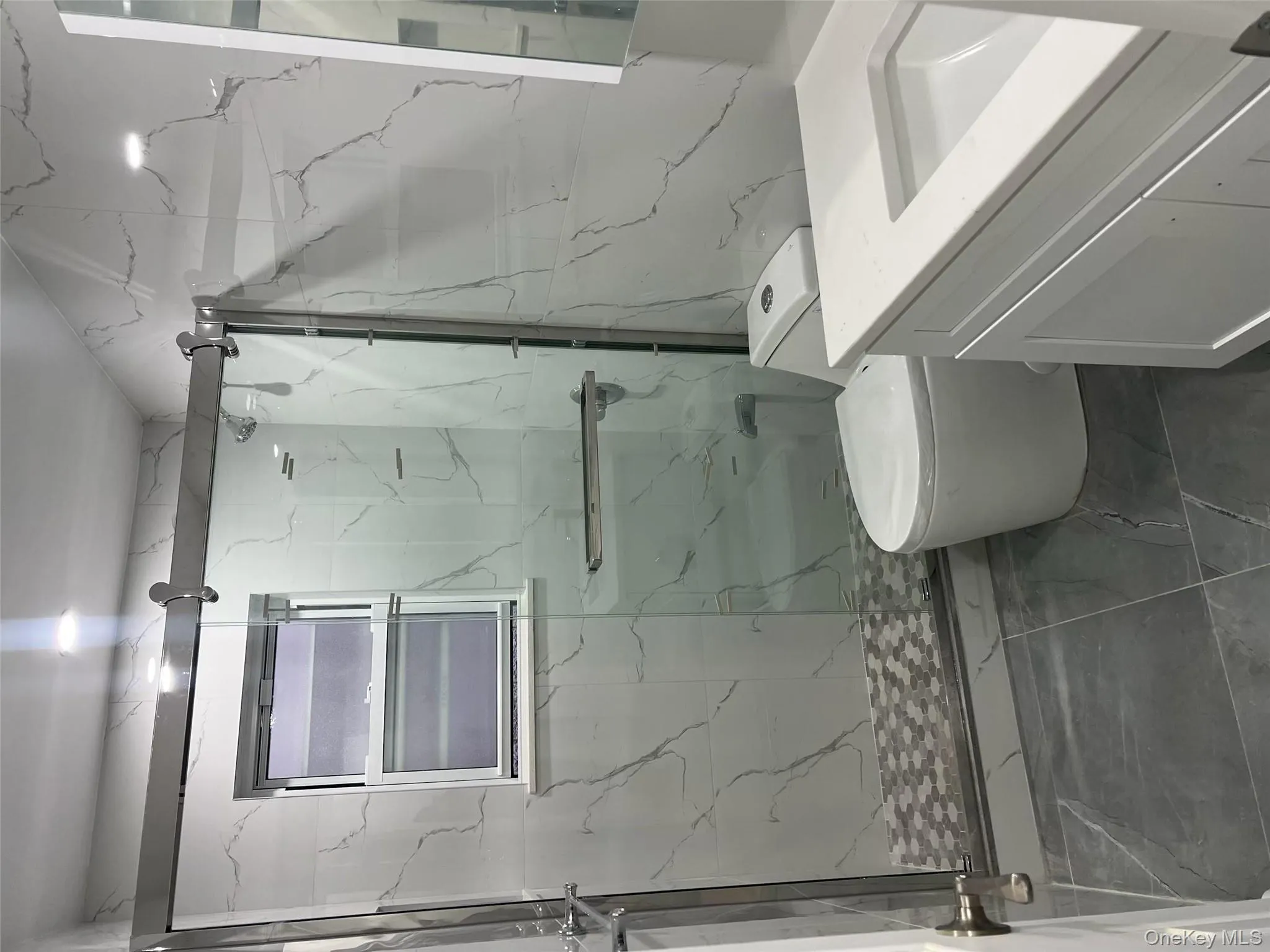 Bathroom featuring vanity, dark marble finish flooring, a marble finish shower, tile walls, and stone wall Bathroom featuring vanity, dark marble finish flooring, a marble finish shower, tile walls, and stone wall