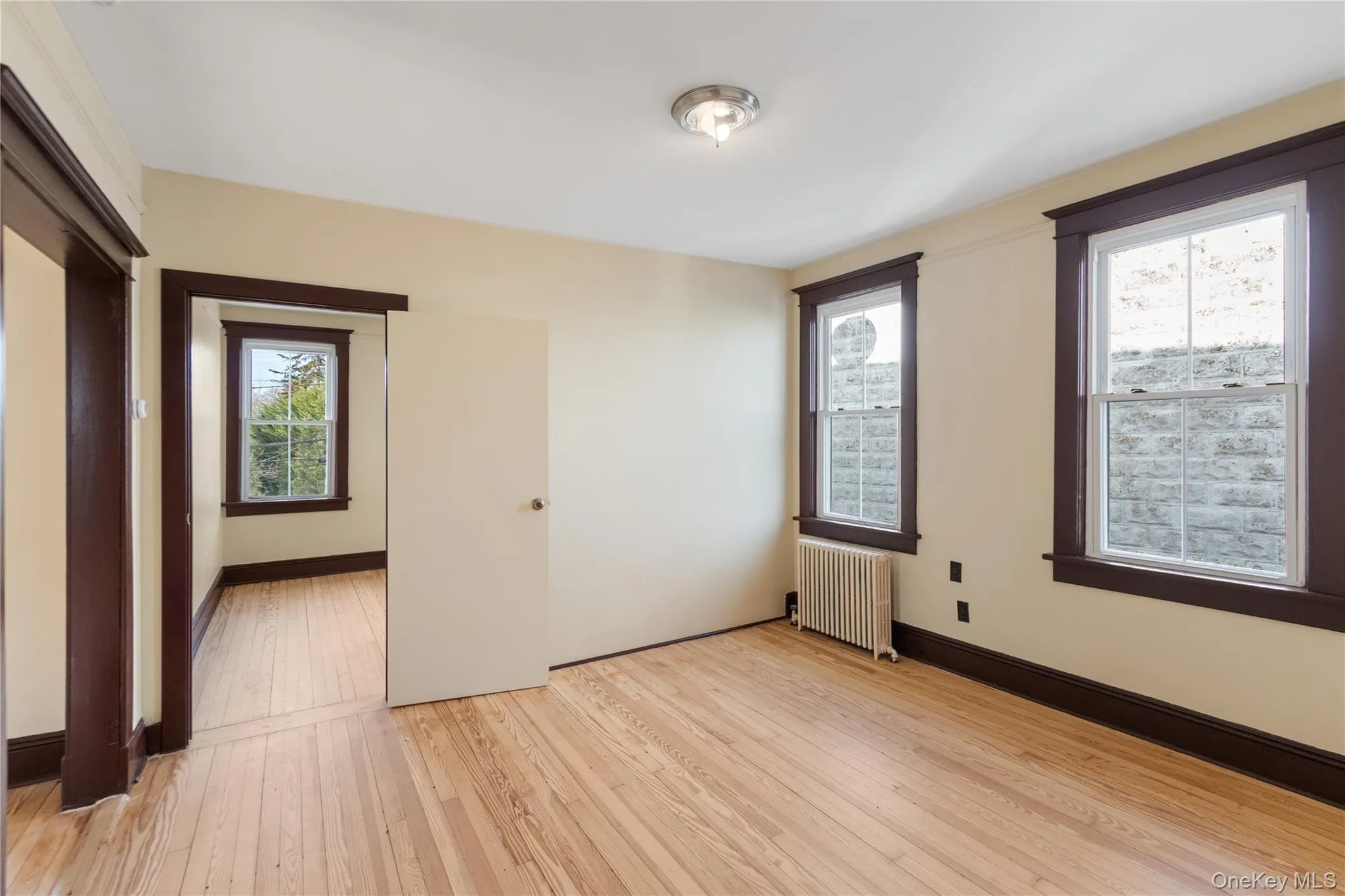 Unfurnished room with radiator, light wood finished floors, and healthy amount of natural light Unfurnished room with radiator, light wood finished floors, and healthy amount of natural light