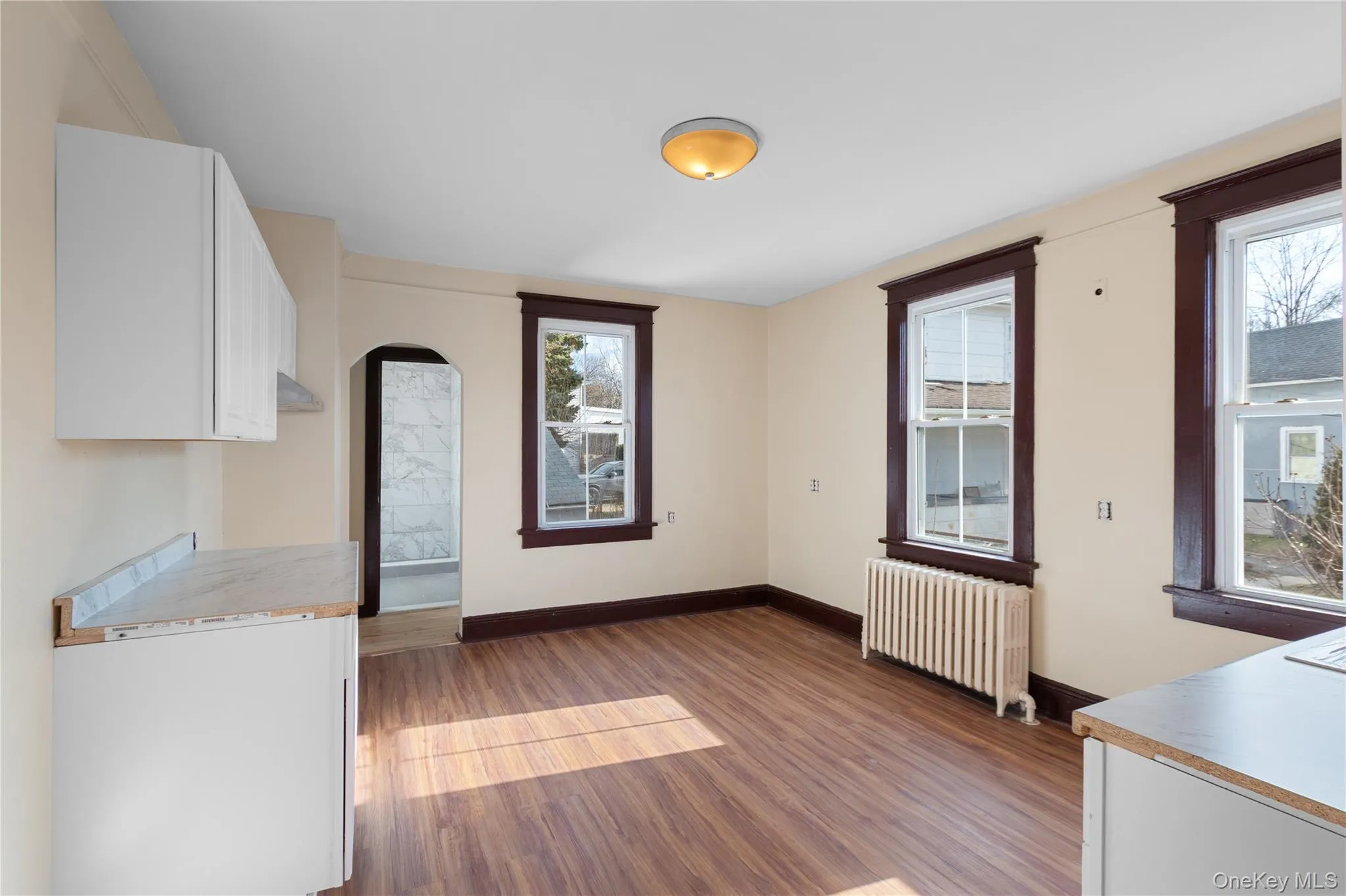 Unfurnished dining area featuring radiator, dark wood-style flooring, and arched walkways Unfurnished dining area featuring radiator, dark wood-style flooring, and arched walkways
