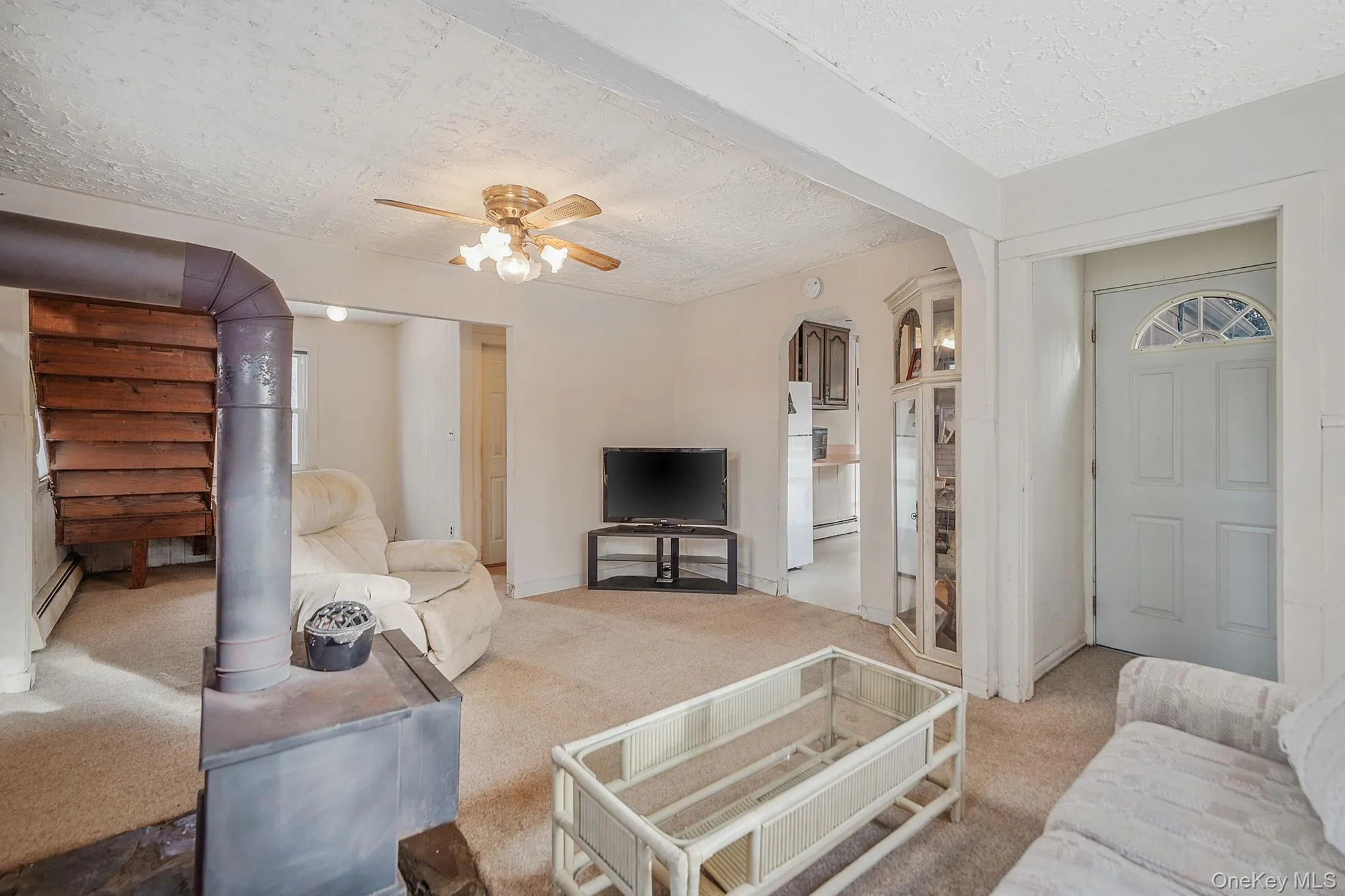 Carpeted living area with ceiling fan, arched walkways, a textured ceiling, and a baseboard heating unit Carpeted living area with ceiling fan, arched walkways, a textured ceiling, and a baseboard heating unit