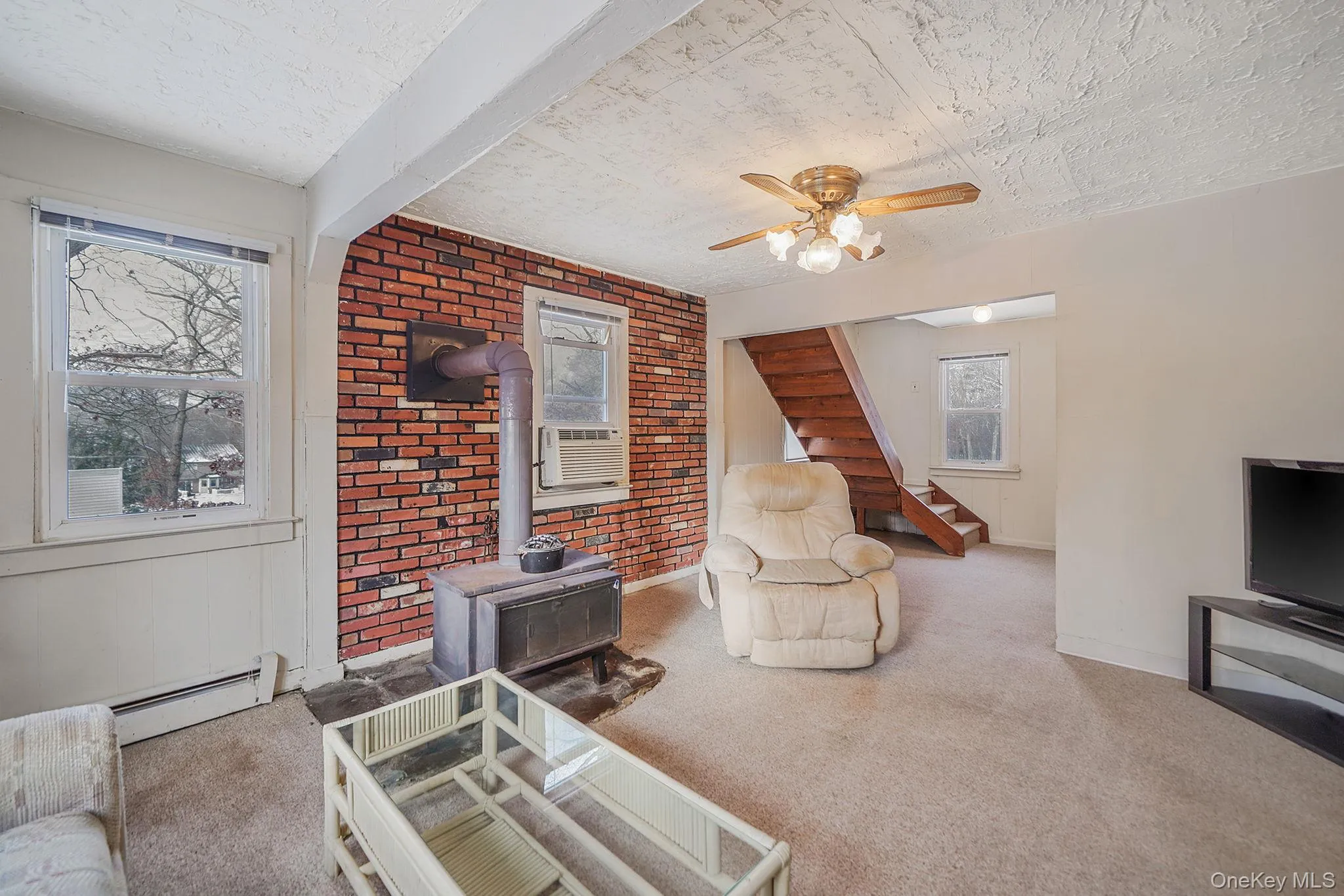 Carpeted living area with a wood stove, brick wall, healthy amount of natural light, a ceiling fan, and baseboard heating Carpeted living area with a wood stove, brick wall, healthy amount of natural light, a ceiling fan, and baseboard heating