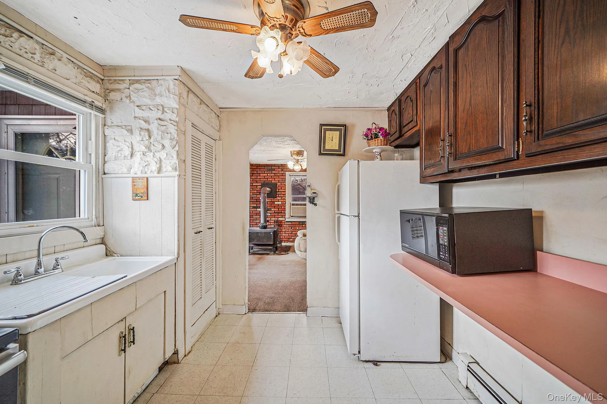 Kitchen featuring ceiling fan, light countertops, a wood stove, freestanding refrigerator, and a textured ceiling Kitchen featuring ceiling fan, light countertops, a wood stove, freestanding refrigerator, and a textured ceiling