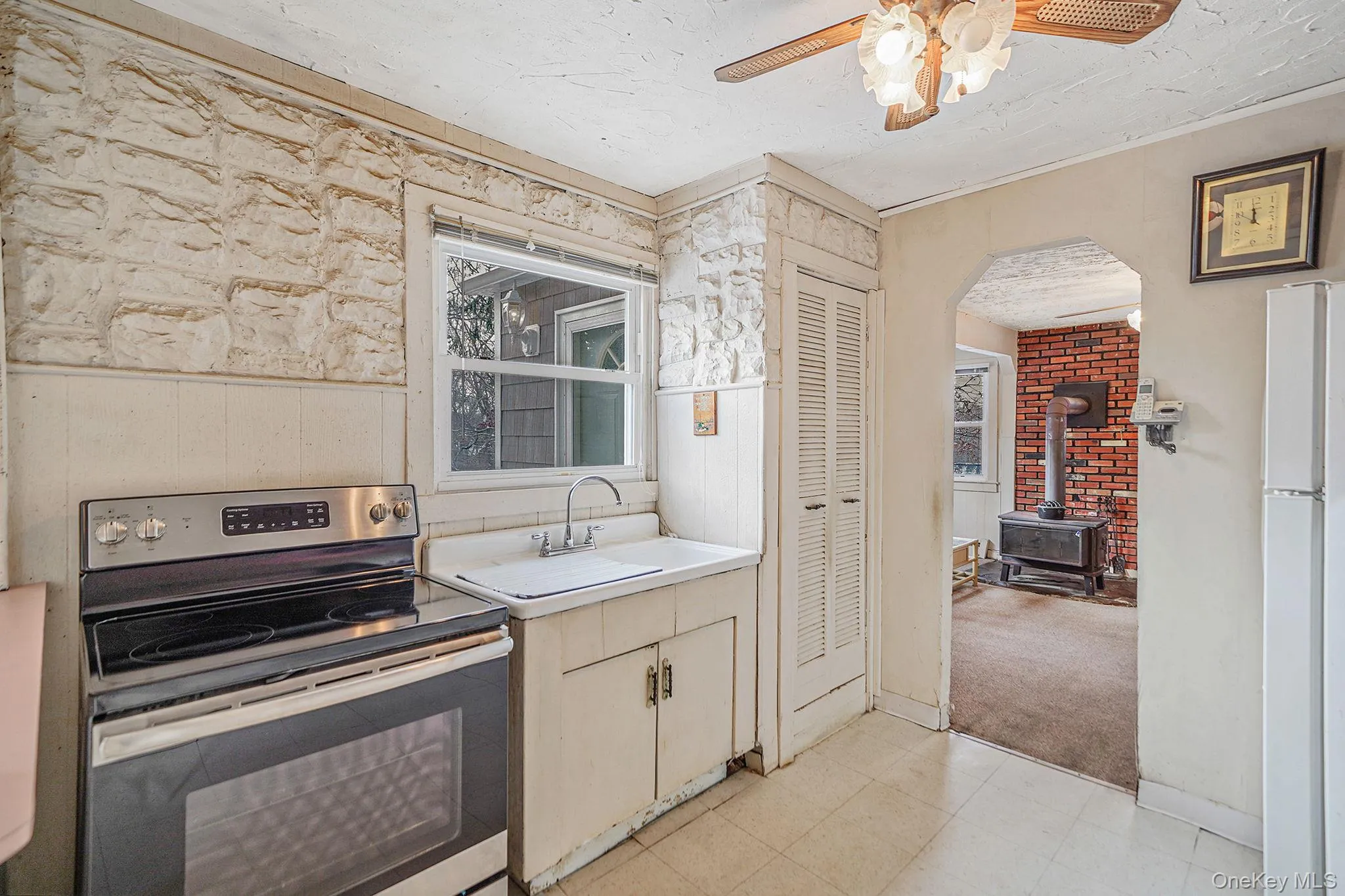 Kitchen featuring stainless steel range with electric cooktop, light countertops, freestanding refrigerator, a wood stove, and a ceiling fan Kitchen featuring stainless steel range with electric cooktop, light countertops, freestanding refrigerator, a wood stove, and a ceiling fan
