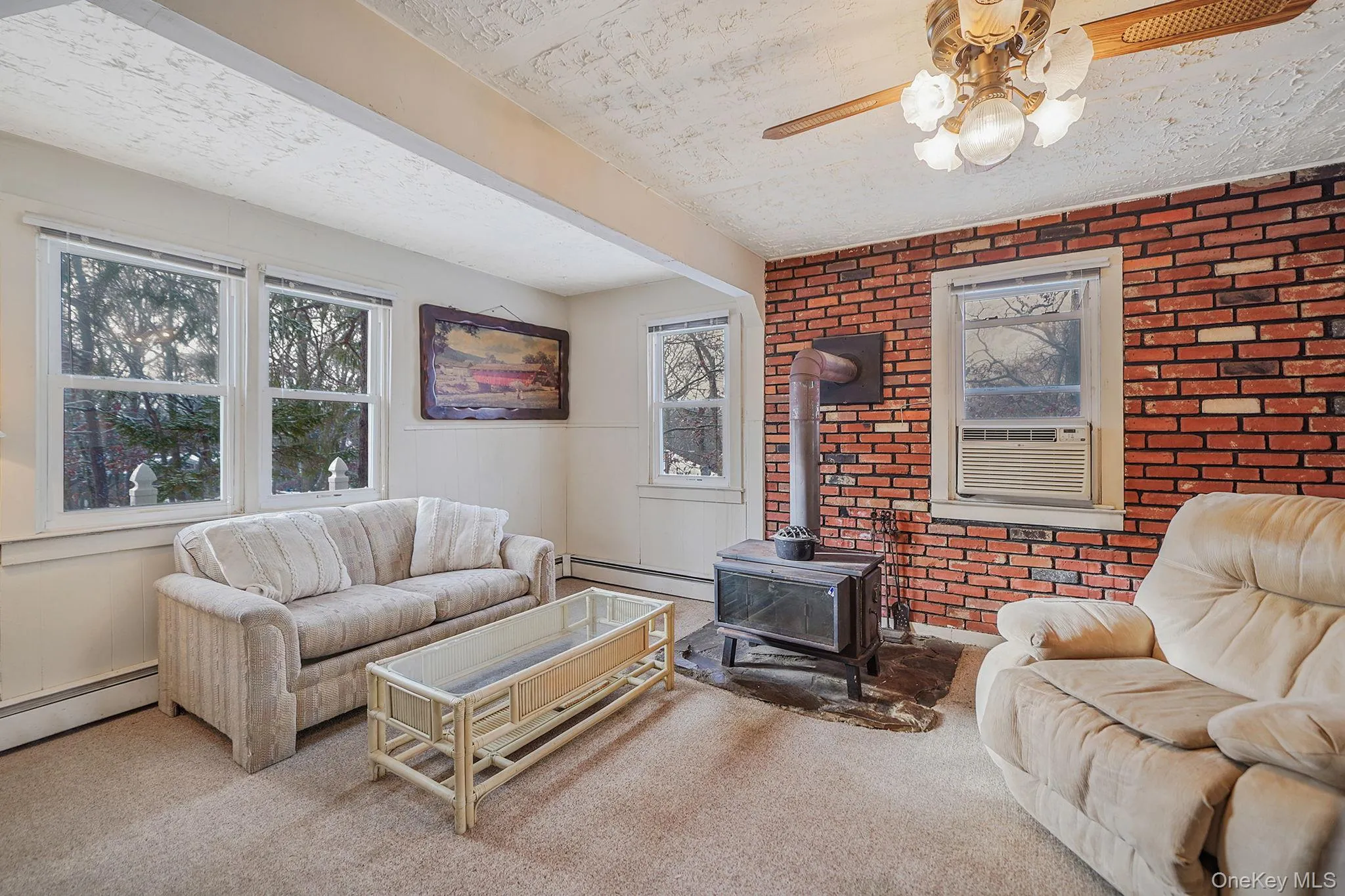 Carpeted living room with brick wall, a wood stove, a baseboard radiator, and ceiling fan Carpeted living room with brick wall, a wood stove, a baseboard radiator, and ceiling fan