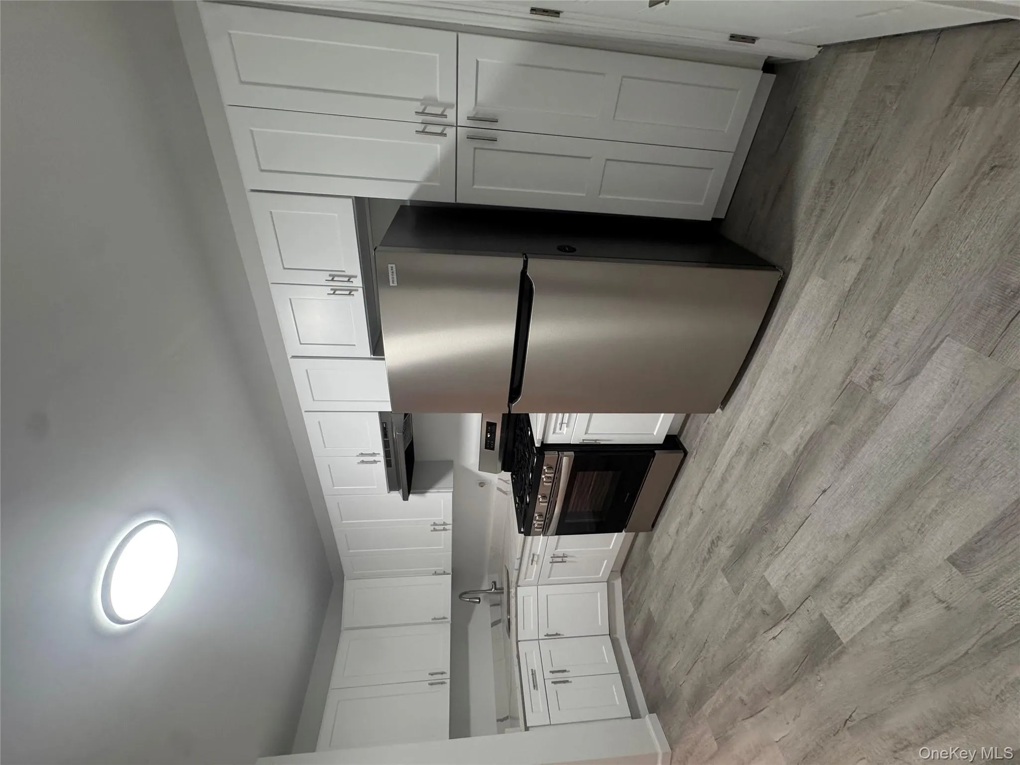 Kitchen featuring stainless steel appliances, white cabinetry, light wood finished floors, and range hood Kitchen featuring stainless steel appliances, white cabinetry, light wood finished floors, and range hood