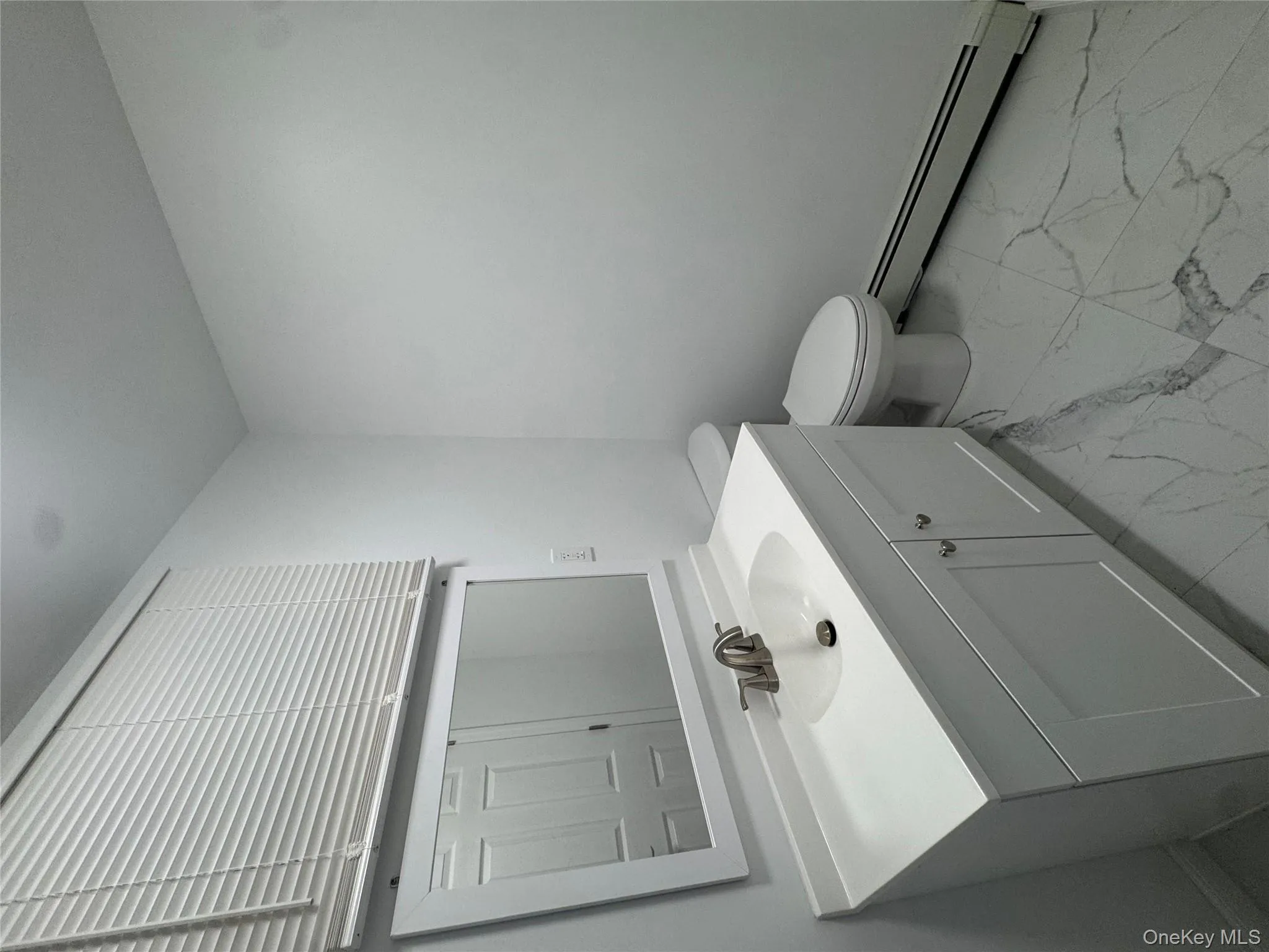 Half bathroom with a baseboard heating unit, vanity, and light marble finish flooring Half bathroom with a baseboard heating unit, vanity, and light marble finish flooring