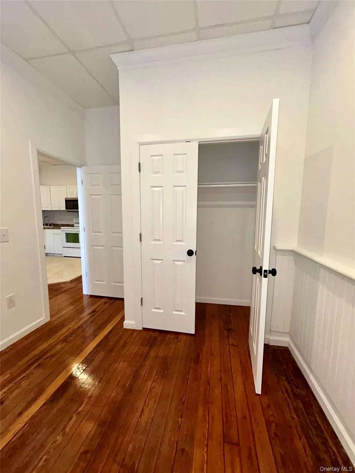 Unfurnished bedroom featuring a drop ceiling, dark wood-type flooring, and a closet Unfurnished bedroom featuring a drop ceiling, dark wood-type flooring, and a closet