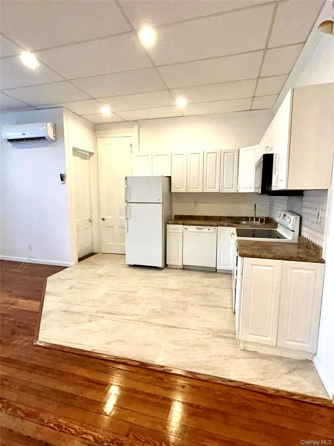 Kitchen with dark countertops, a drop ceiling, white cabinets, white appliances, and light wood-style flooring Kitchen with dark countertops, a drop ceiling, white cabinets, white appliances, and light wood-style flooring