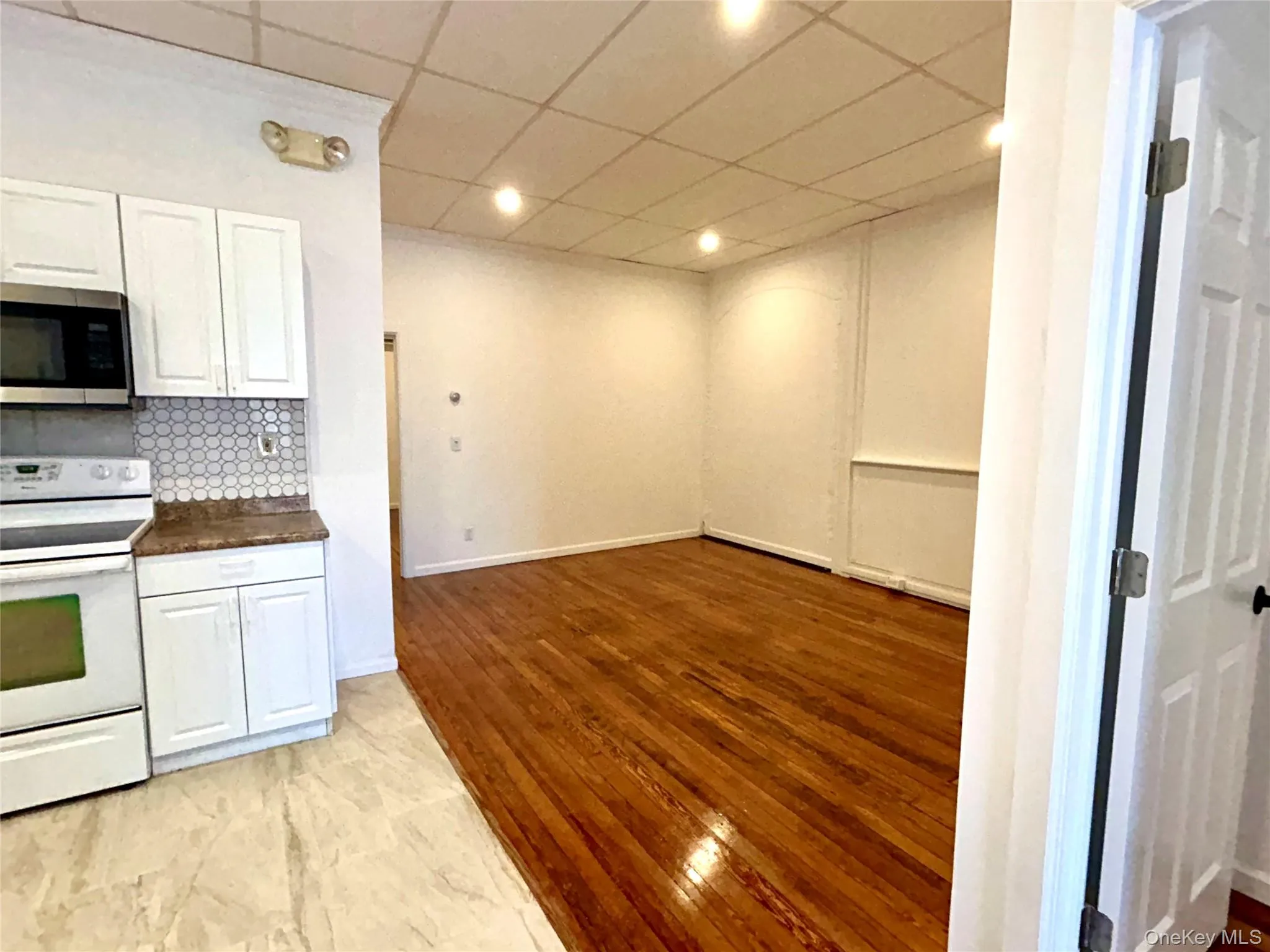 Kitchen with electric range, white cabinets, a paneled ceiling, stainless steel microwave, and light wood-style flooring Kitchen with electric range, white cabinets, a paneled ceiling, stainless steel microwave, and light wood-style flooring