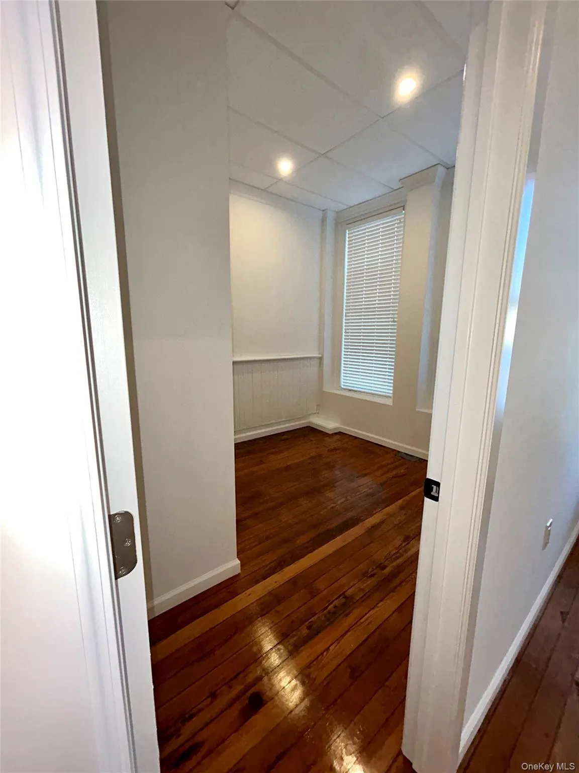 Empty room featuring dark wood-style flooring, a wainscoted wall, and recessed lighting Empty room featuring dark wood-style flooring, a wainscoted wall, and recessed lighting