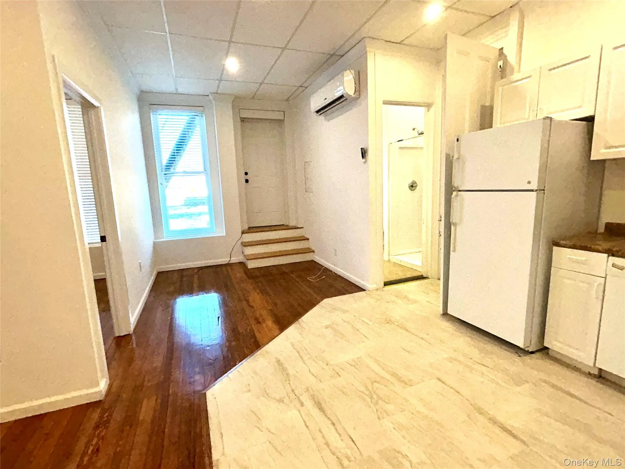 Kitchen featuring a paneled ceiling, white appliances, white cabinetry, dark wood finished floors, and a wall unit AC Kitchen featuring a paneled ceiling, white appliances, white cabinetry, dark wood finished floors, and a wall unit AC