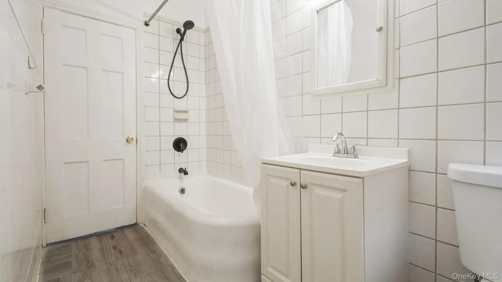 Full bathroom featuring shower / tub combo, tile walls, vanity, and dark wood-type flooring Full bathroom featuring shower / tub combo, tile walls, vanity, and dark wood-type flooring