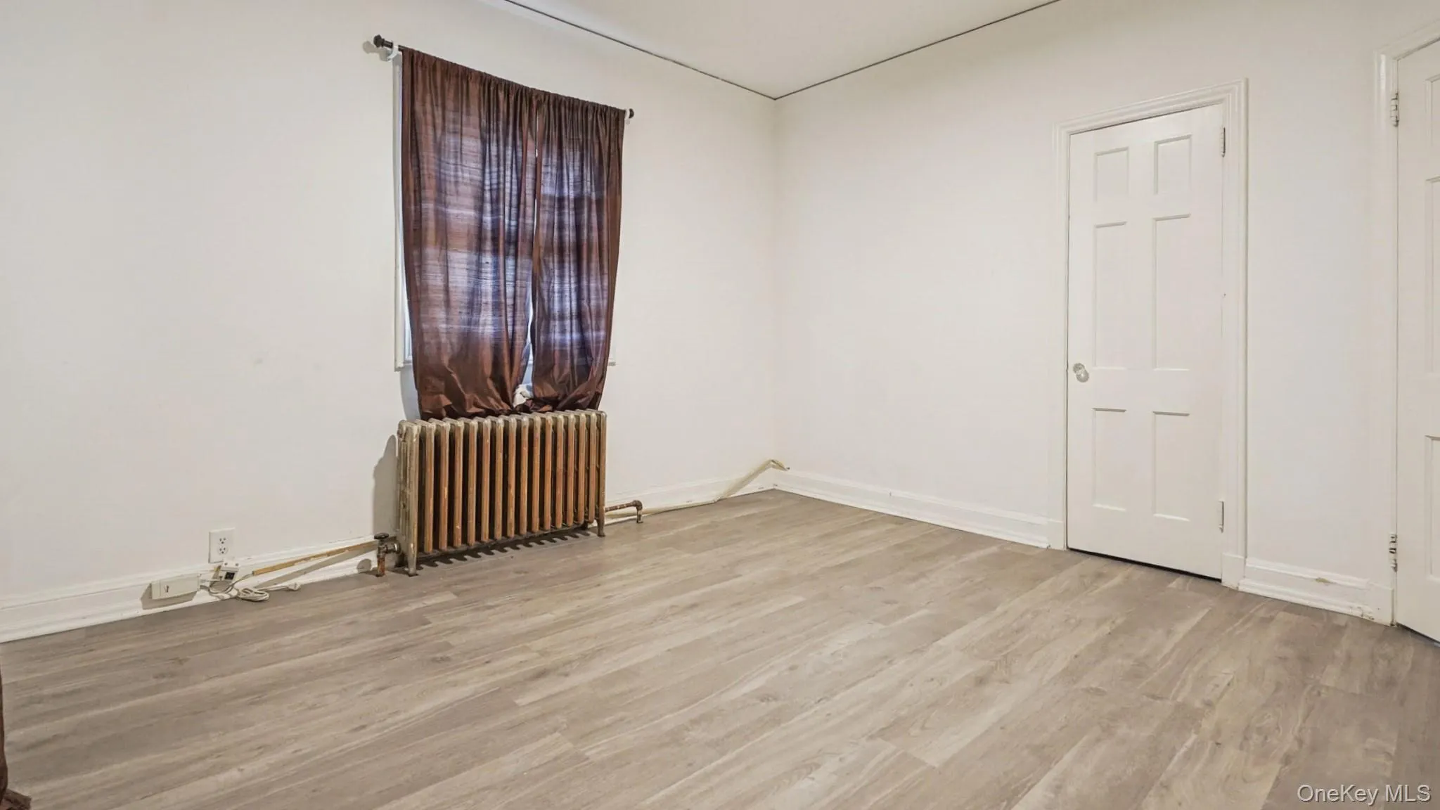 Unfurnished room with radiator heating unit and light wood-style floors Unfurnished room with radiator heating unit and light wood-style floors