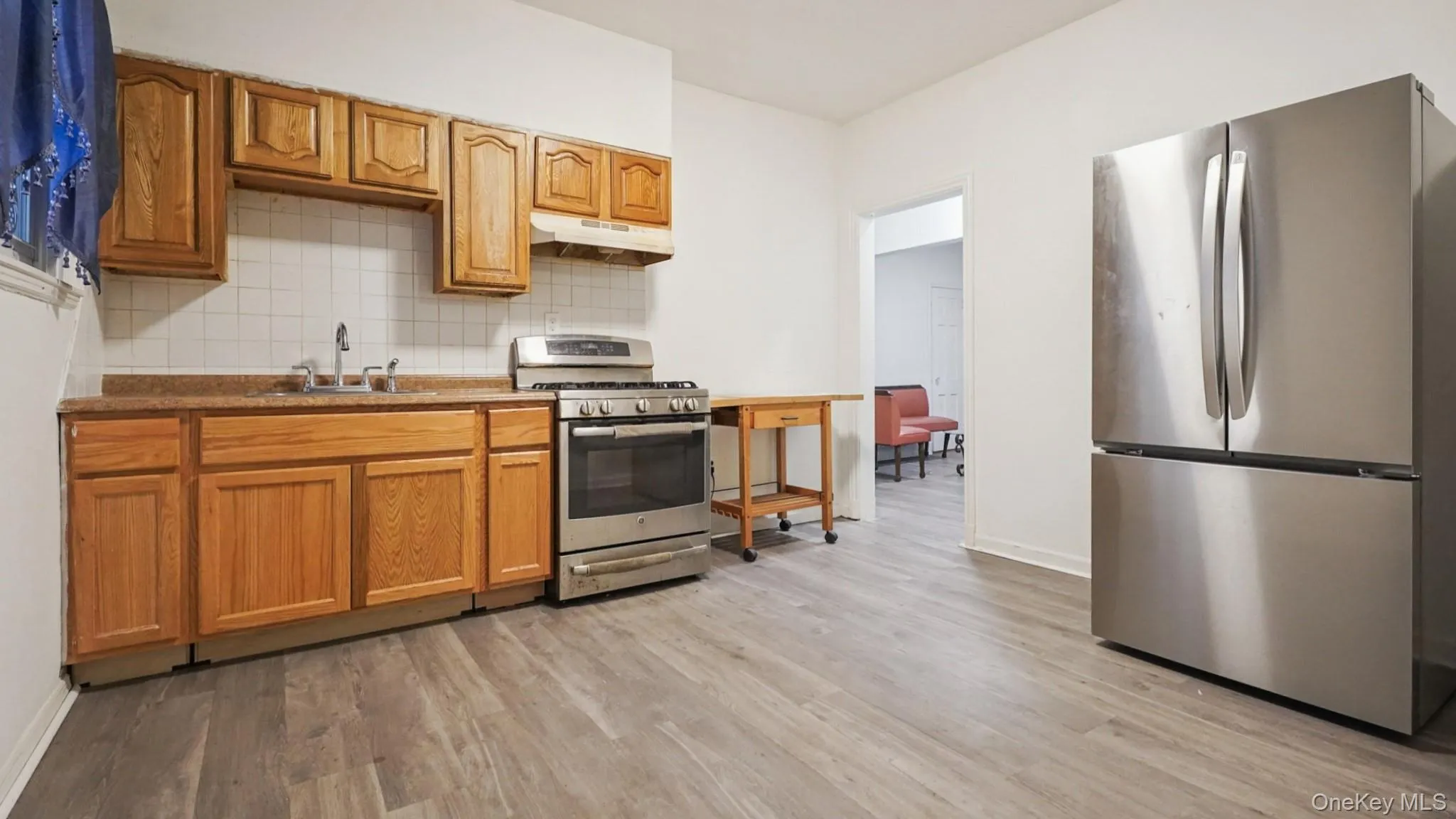 Kitchen featuring appliances with stainless steel finishes, backsplash, under cabinet range hood, brown cabinets, and light wood finished floors Kitchen featuring appliances with stainless steel finishes, backsplash, under cabinet range hood, brown cabinets, and light wood finished floors