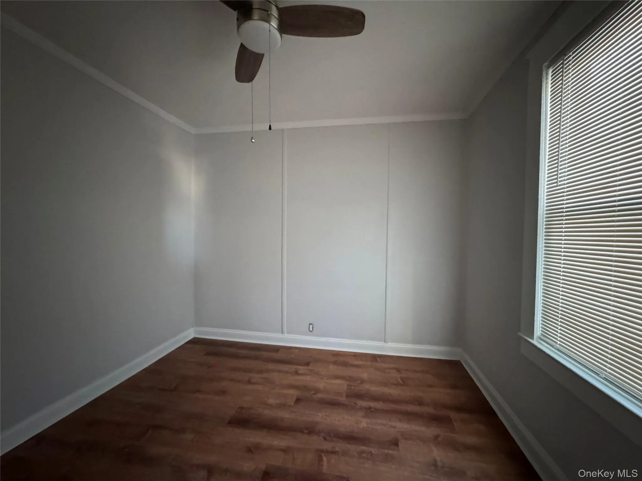 Empty room with a ceiling fan, dark wood-style flooring, and crown molding Empty room with a ceiling fan, dark wood-style flooring, and crown molding