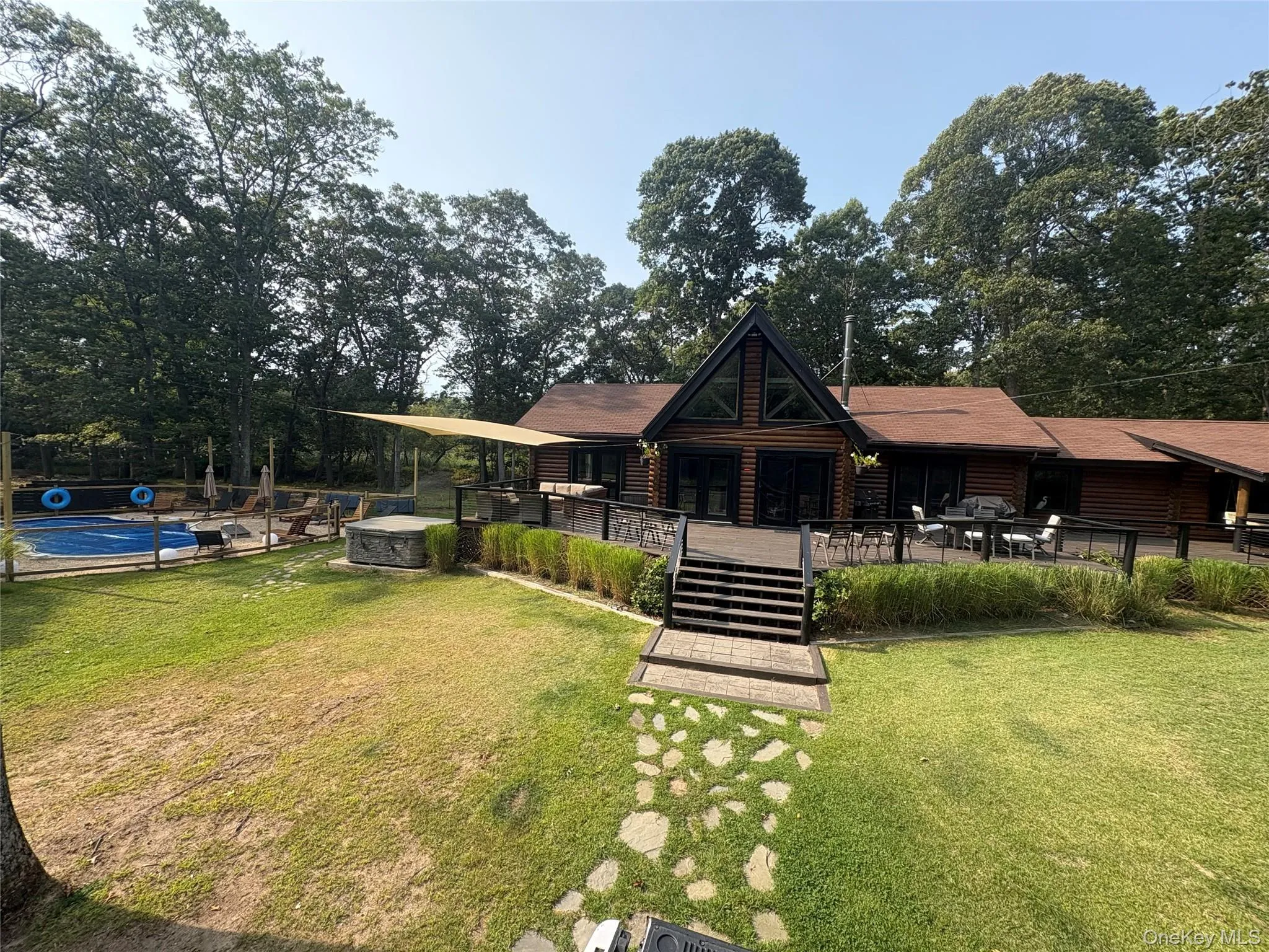 Rear view of house featuring an outdoor pool, a patio, faux log siding, and view of scattered trees Rear view of house featuring an outdoor pool, a patio, faux log siding, and view of scattered trees