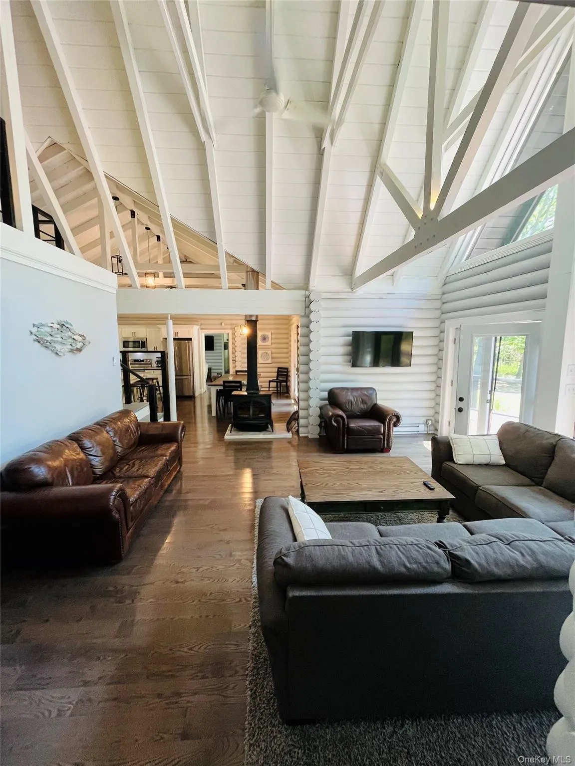 Living area featuring high vaulted ceiling, beam ceiling, hardwood / wood-style flooring, and a wood stove Living area featuring high vaulted ceiling, beam ceiling, hardwood / wood-style flooring, and a wood stove