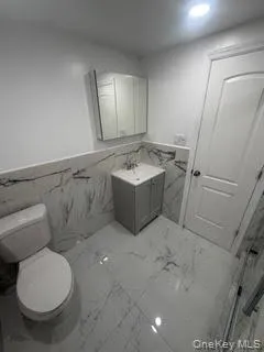 Bathroom with a wainscoted wall, tile walls, vanity, marble tiled flooring, and recessed lighting Bathroom with a wainscoted wall, tile walls, vanity, marble tiled flooring, and recessed lighting