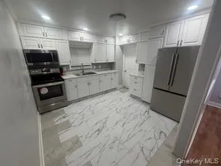 Kitchen featuring appliances with stainless steel finishes, light countertops, white cabinets, light marble finish floors, and recessed lighting Kitchen featuring appliances with stainless steel finishes, light countertops, white cabinets, light marble finish floors, and recessed lighting