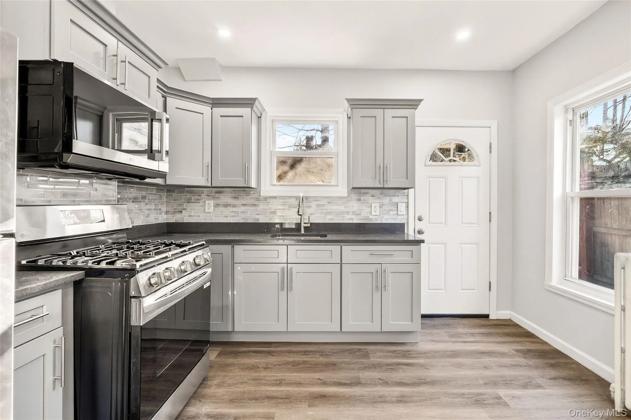 Kitchen with gas range, light wood-style flooring, backsplash, dark stone countertops, and radiator Kitchen with gas range, light wood-style flooring, backsplash, dark stone countertops, and radiator