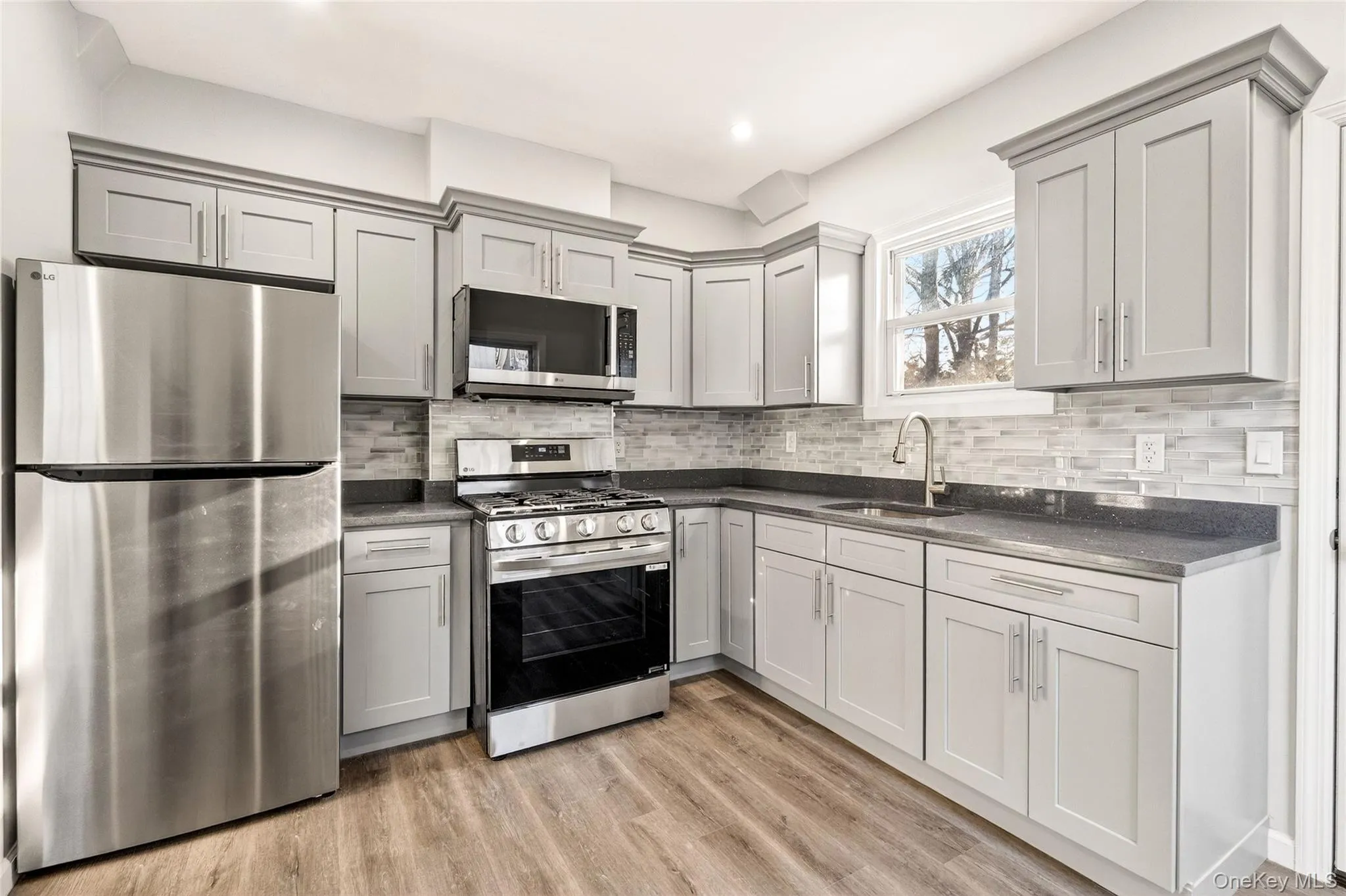 Kitchen with appliances with stainless steel finishes, gray cabinetry, light wood-style flooring, backsplash, and recessed lighting Kitchen with appliances with stainless steel finishes, gray cabinetry, light wood-style flooring, backsplash, and recessed lighting