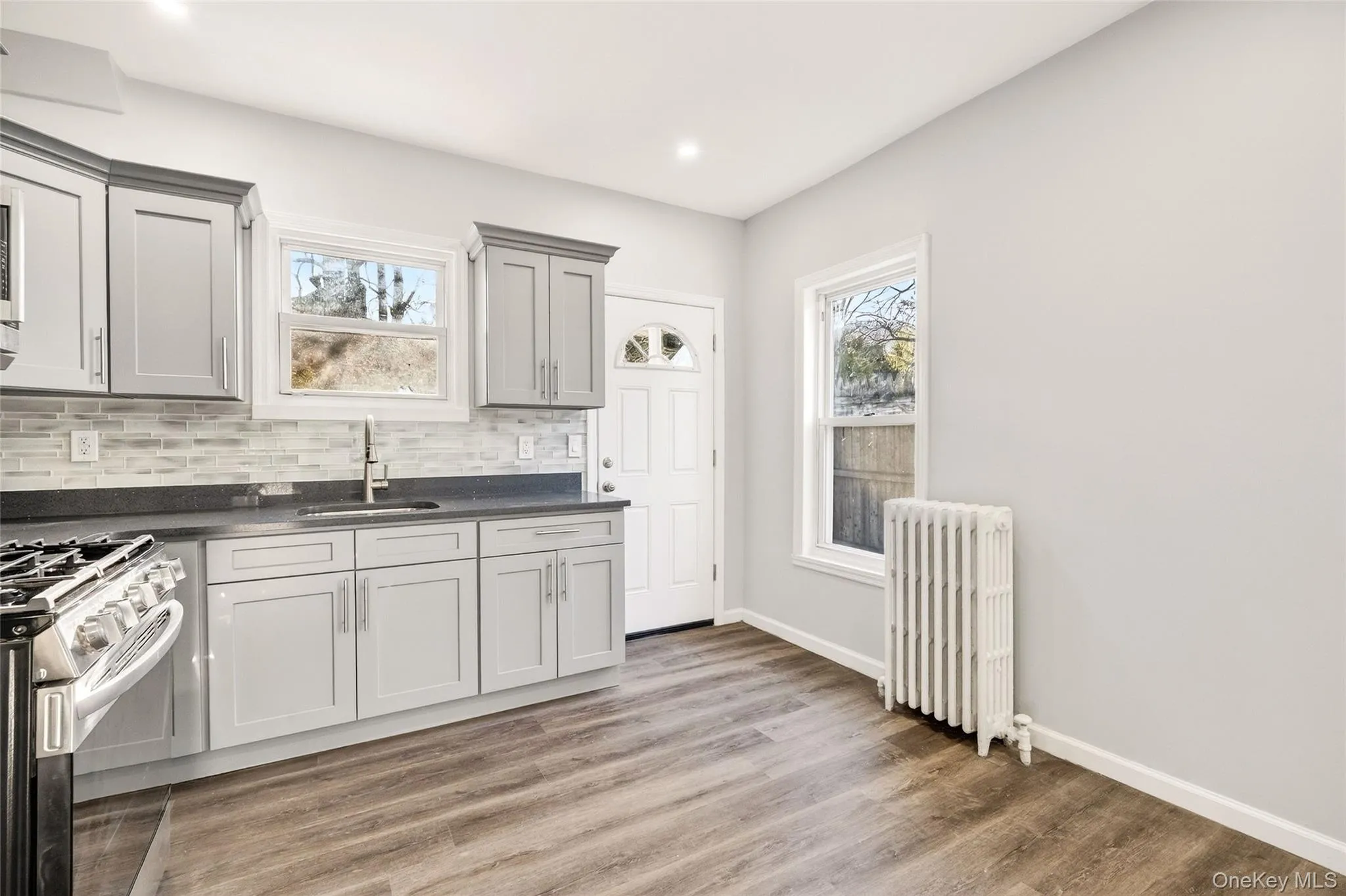 Kitchen featuring radiator, light wood-style flooring, tasteful backsplash, gray cabinetry, and gas range Kitchen featuring radiator, light wood-style flooring, tasteful backsplash, gray cabinetry, and gas range
