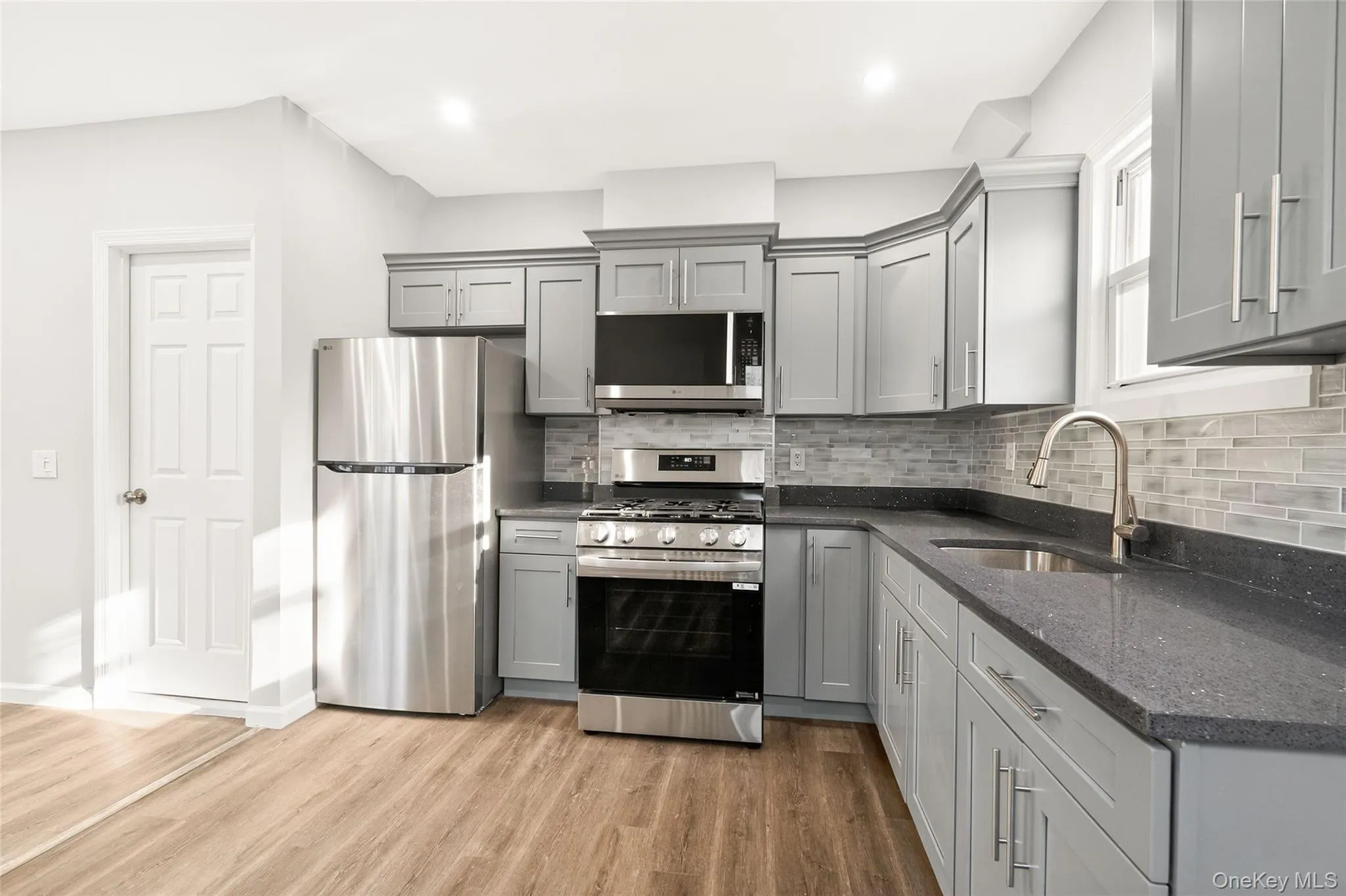 Kitchen featuring appliances with stainless steel finishes, gray cabinetry, dark stone countertops, light wood-type flooring, and recessed lighting Kitchen featuring appliances with stainless steel finishes, gray cabinetry, dark stone countertops, light wood-type flooring, and recessed lighting