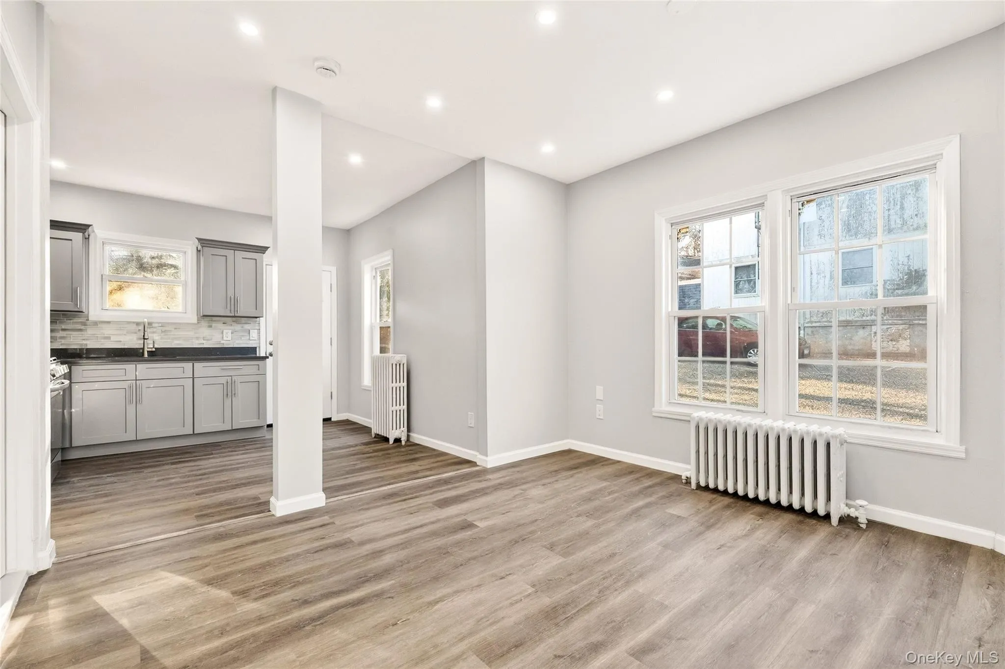 Unfurnished living room with radiator heating unit, healthy amount of natural light, light wood-type flooring, and recessed lighting Unfurnished living room with radiator heating unit, healthy amount of natural light, light wood-type flooring, and recessed lighting
