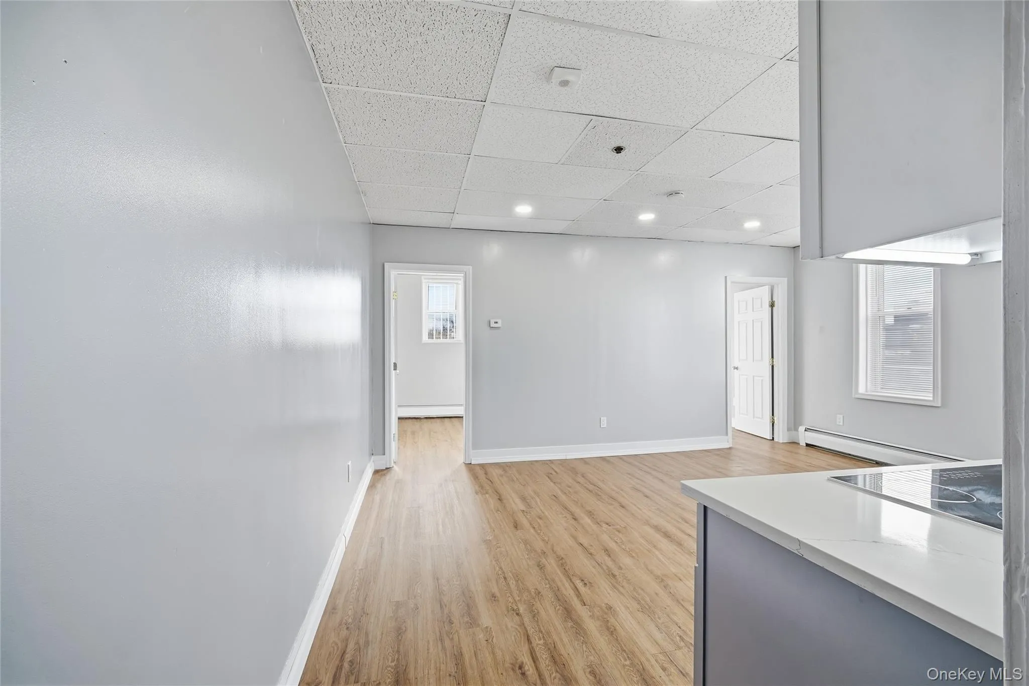 Unfurnished living room with a paneled ceiling, light wood finished floors, and a baseboard heating unit Unfurnished living room with a paneled ceiling, light wood finished floors, and a baseboard heating unit